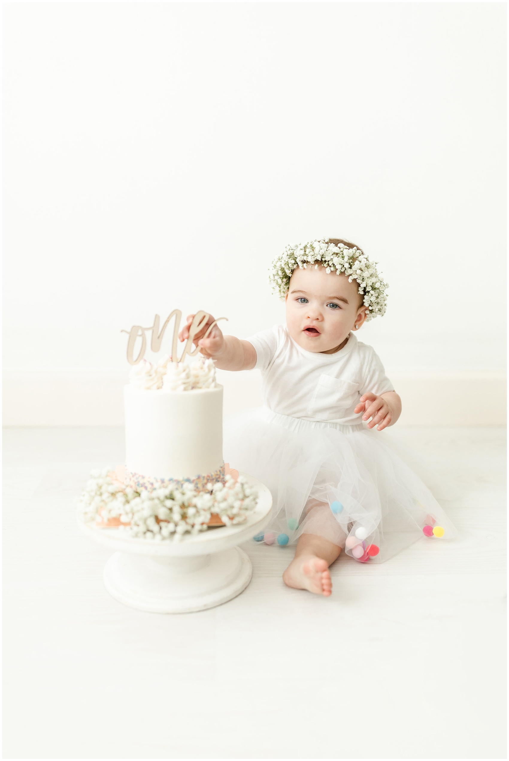 A toddler girl in a white tutu plays with her birthday cake on the floor of a studio after visiting birthday party venues miami