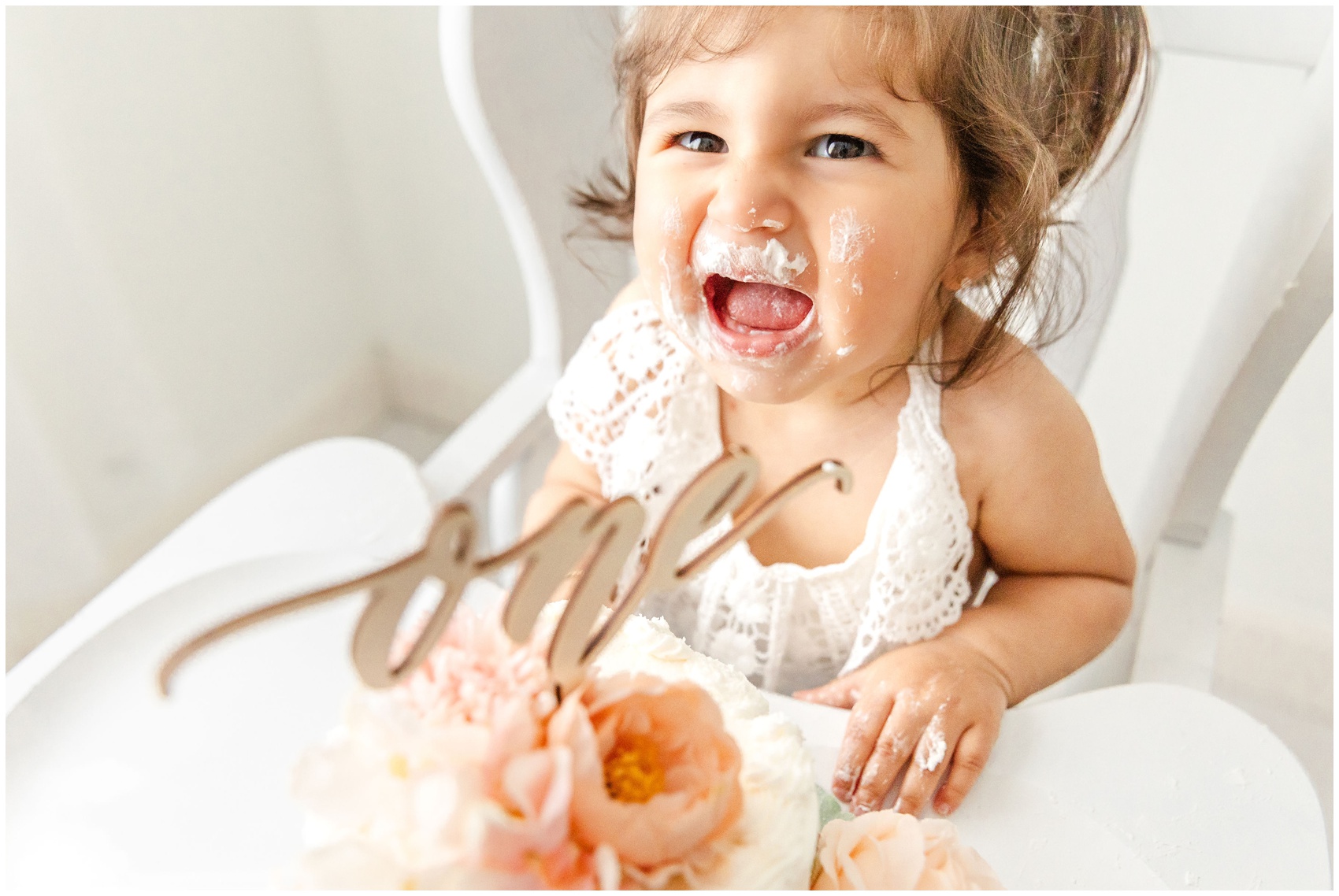 A toddler girl in a lace white dress cries while covered in cake in a high chair after visiting birthday party venues miami