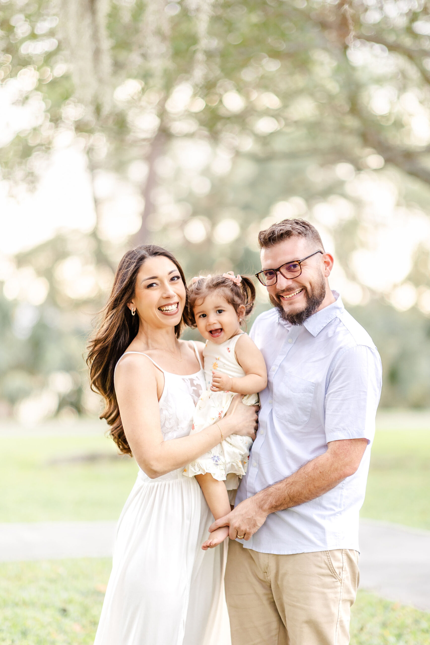 A happy family of 3 laugh while exploring a park at sunset before visiting christmas lights in miami