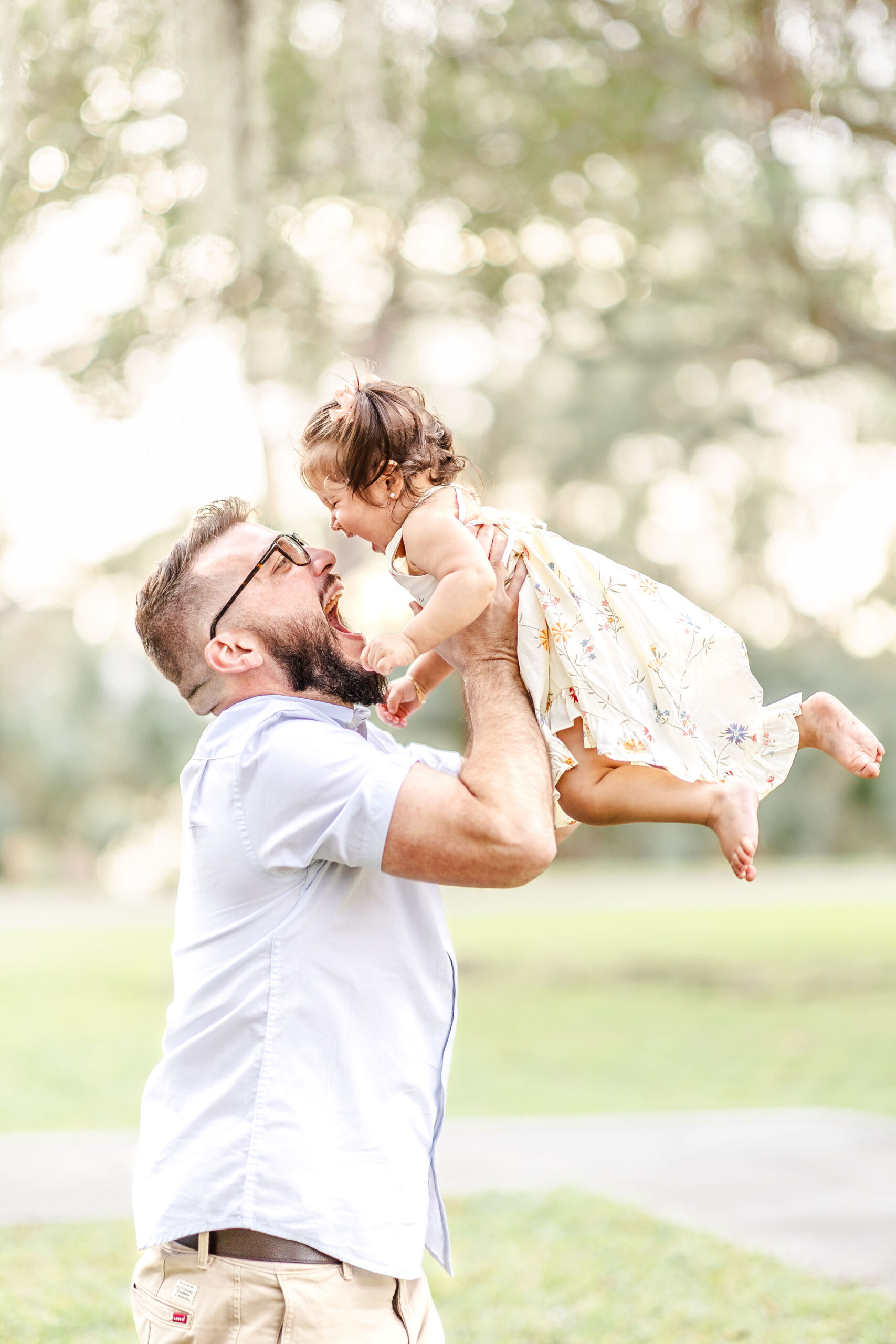 A laughing toddler girl is lifted by her happy dad while playing in a park before exploring christmas lights in miami