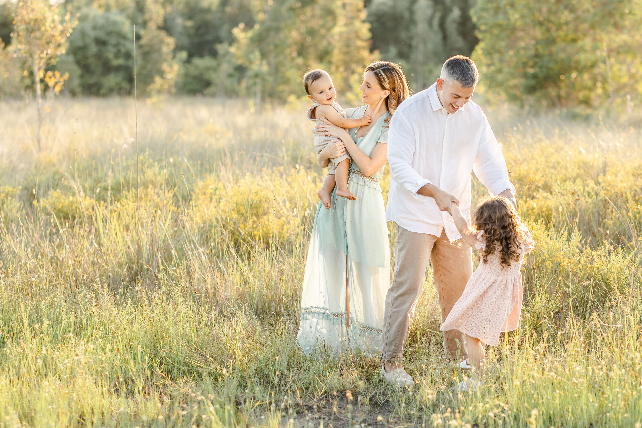 A happy family dances and plays in a field of tall grass at sunset