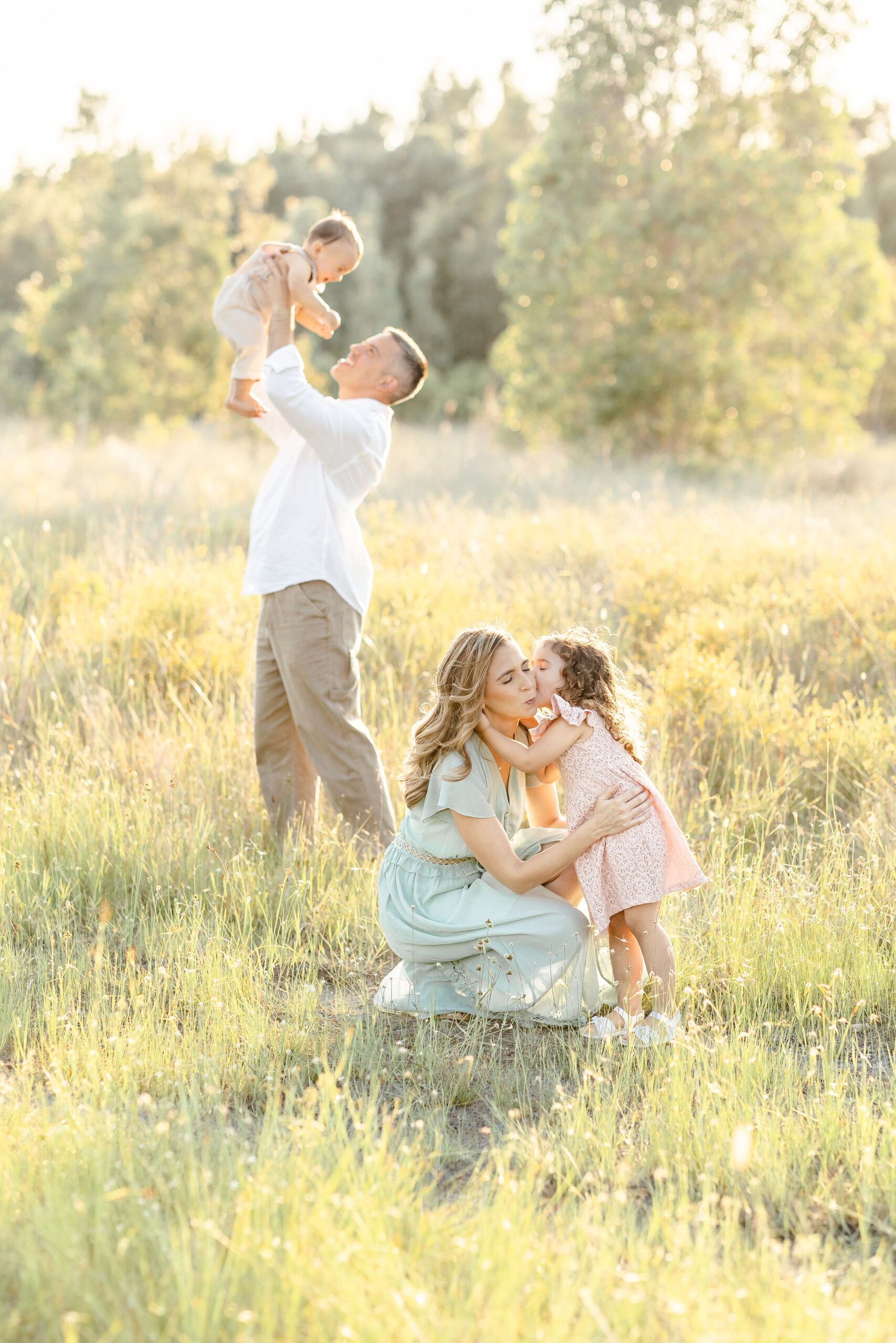 A happy family of 4 with 2 young toddlers play in a park field of tall grass at sunset before some holiday events miami