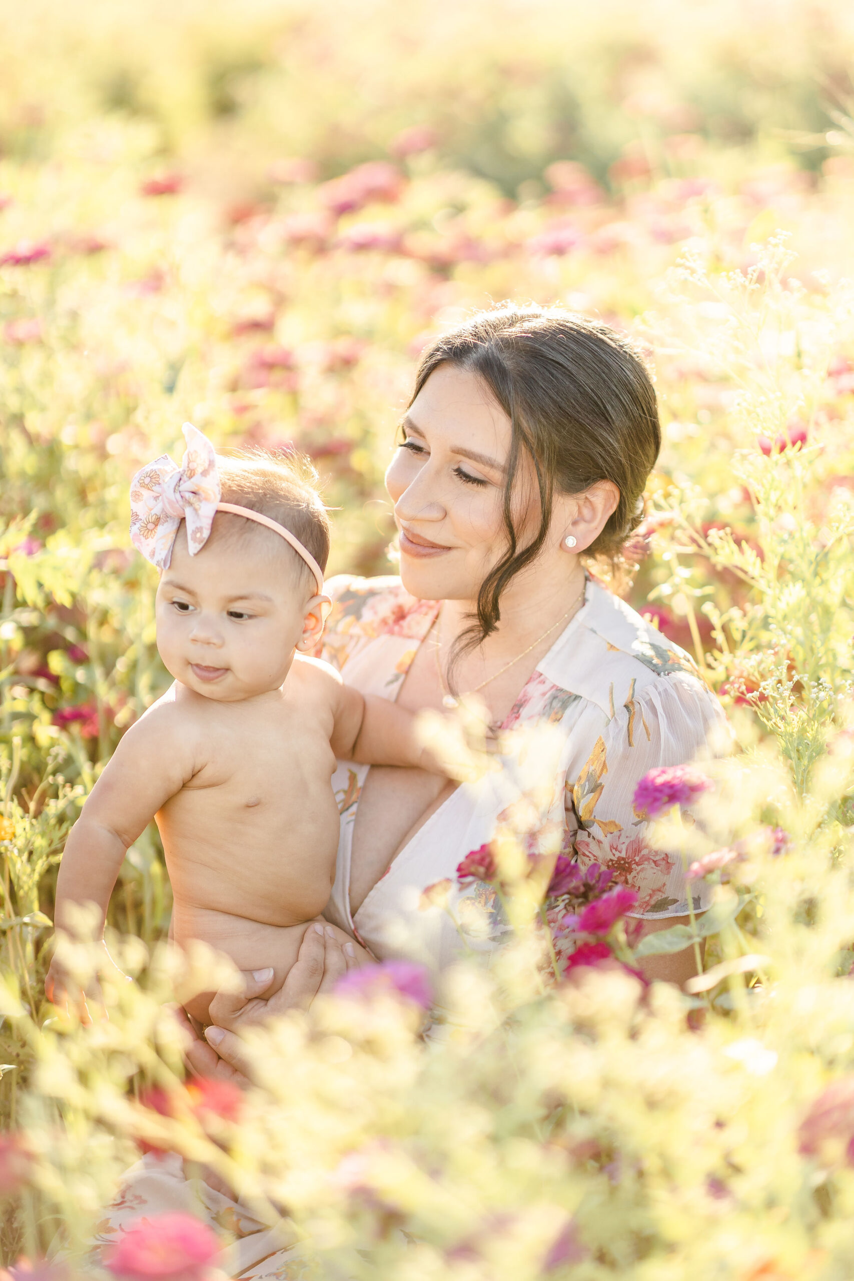 A happy infant girl and smiling mother explore a field of wildflowers at sunset