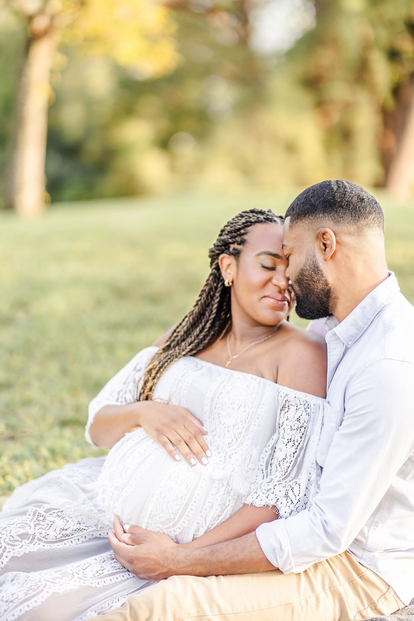 A happy expecting couple snuggles in a park at sunset in white after meeting blooming bellies