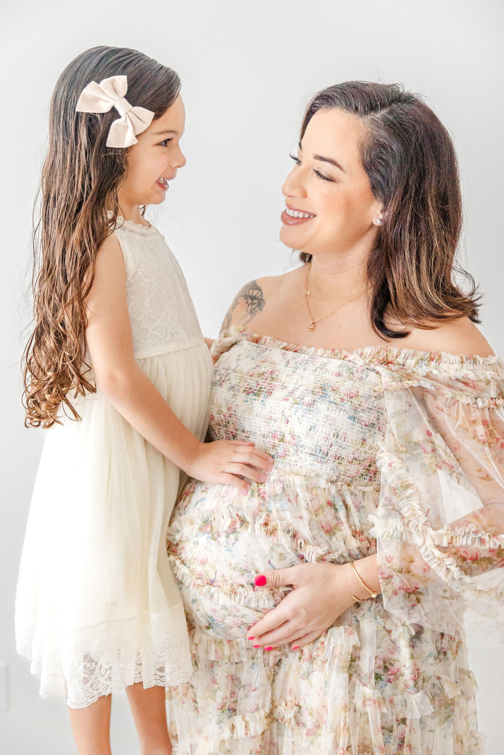 A young girl touches mom's pregnant bump while standing on a bench in a studio after visiting full circle maternity