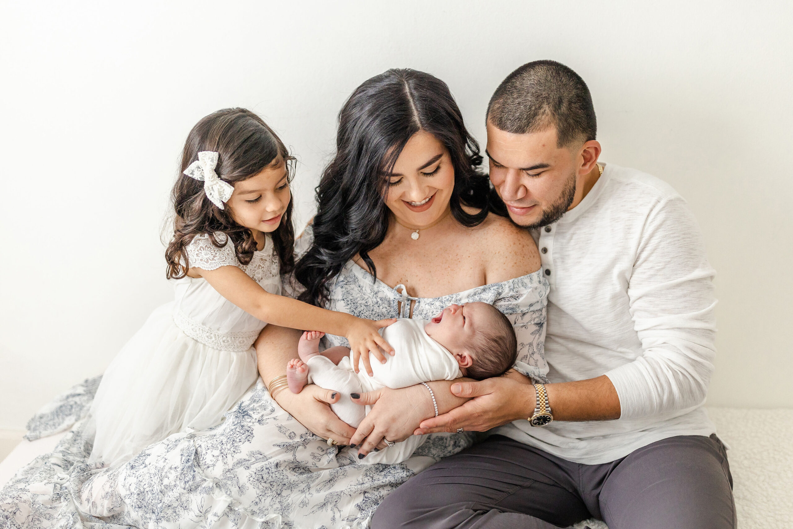 A newborn yawns while mom, dad and older sister smile on