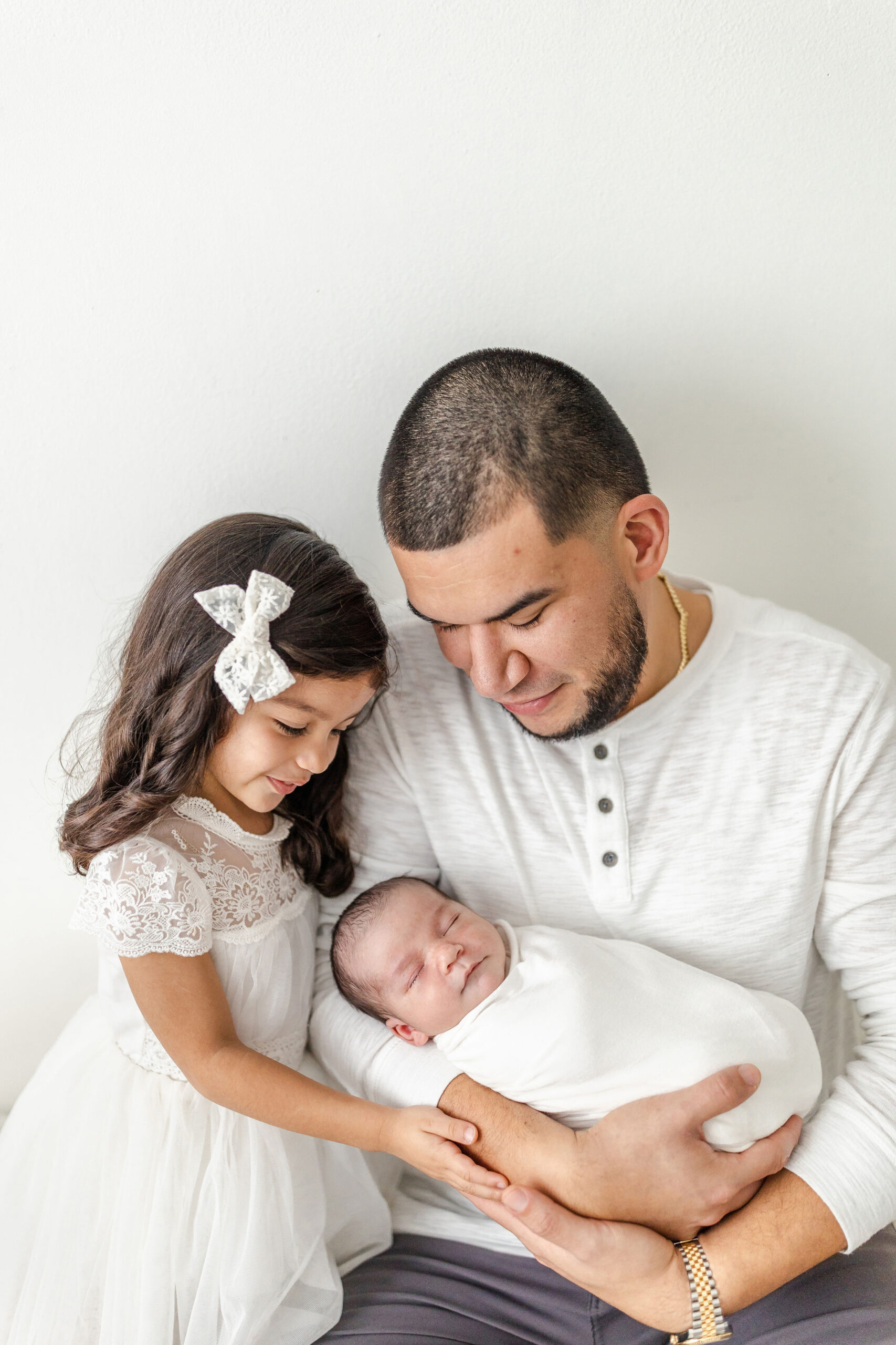 A young girl smiles over her newborn sibling sleeping in dad's arms thanks to a postpartum doula in miami