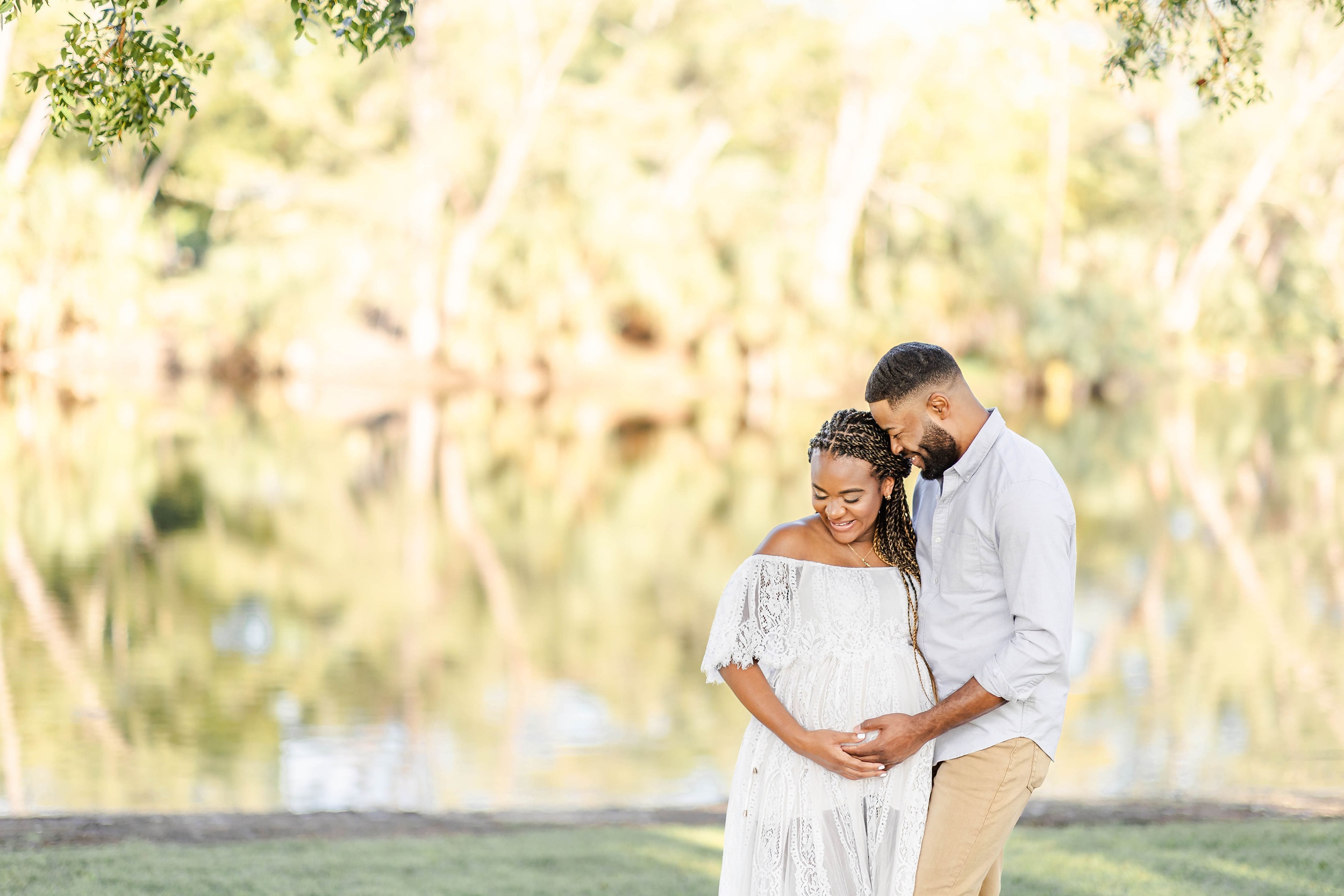 A happy pregnant couple snuggles by a lake with hands on the bump