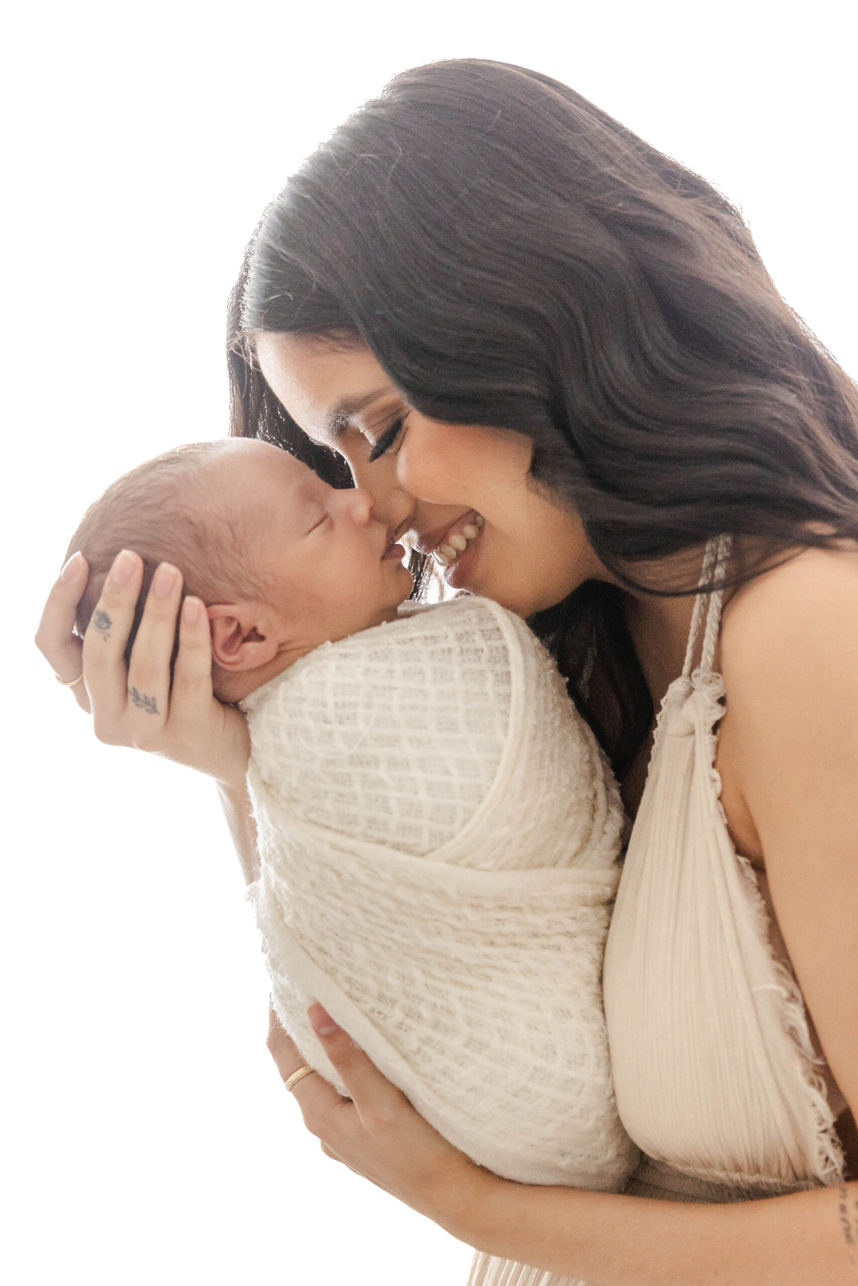 A happy new mom snuggles her sleeping newborn in a tan dress in a studio after finding infant daycare in fort lauderdale