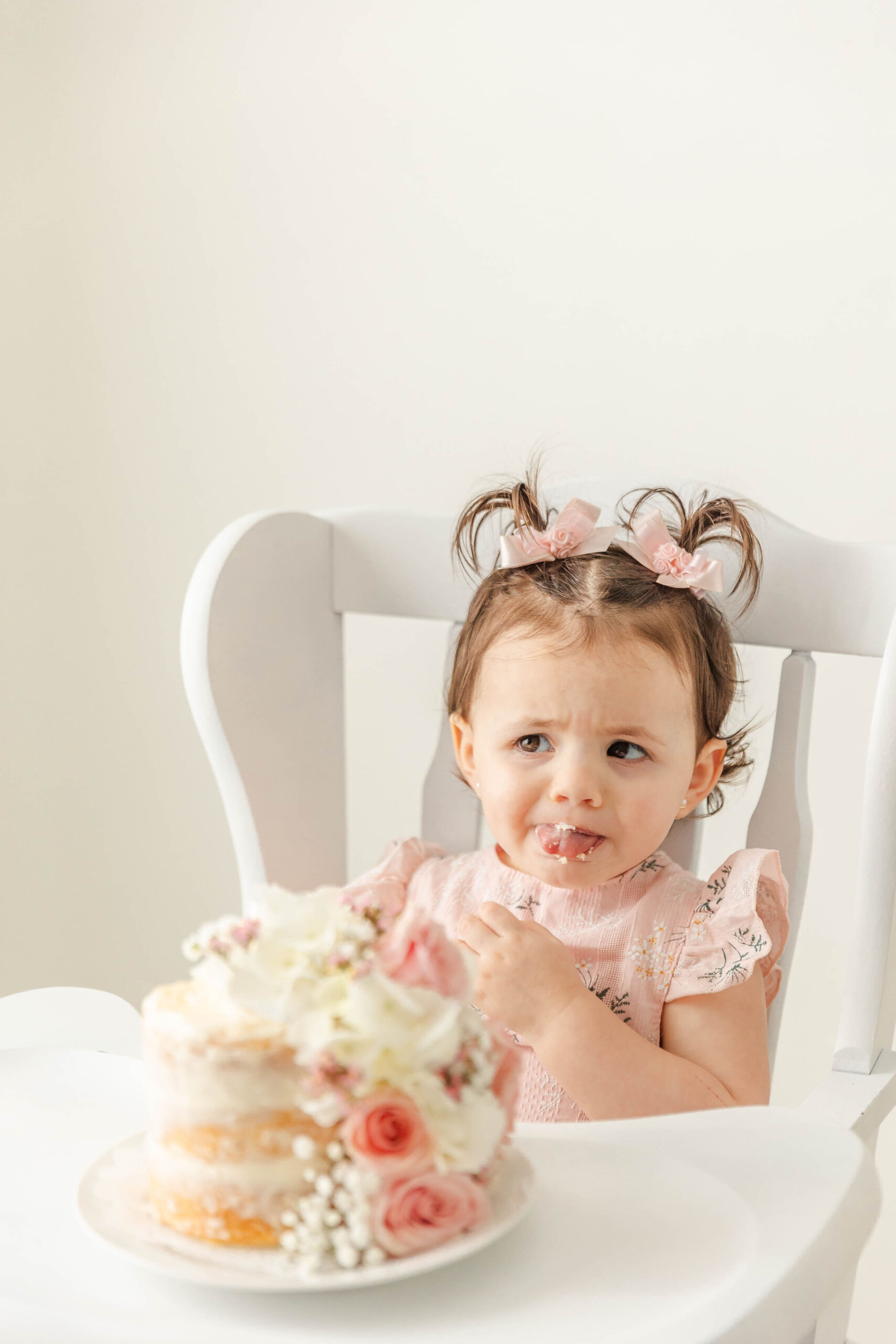A baby girl in a pink dress tastes cake in a white high chair after visiting pediatric dentists in fort lauderdale