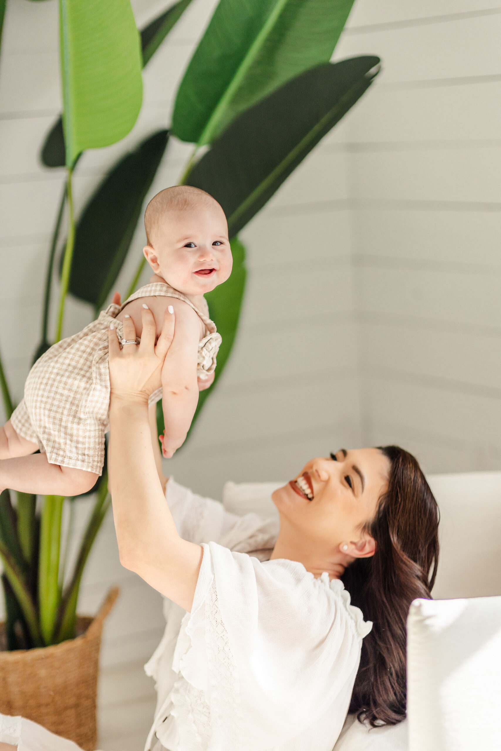A baby smiles big while mom lifts her high in the air in a studio