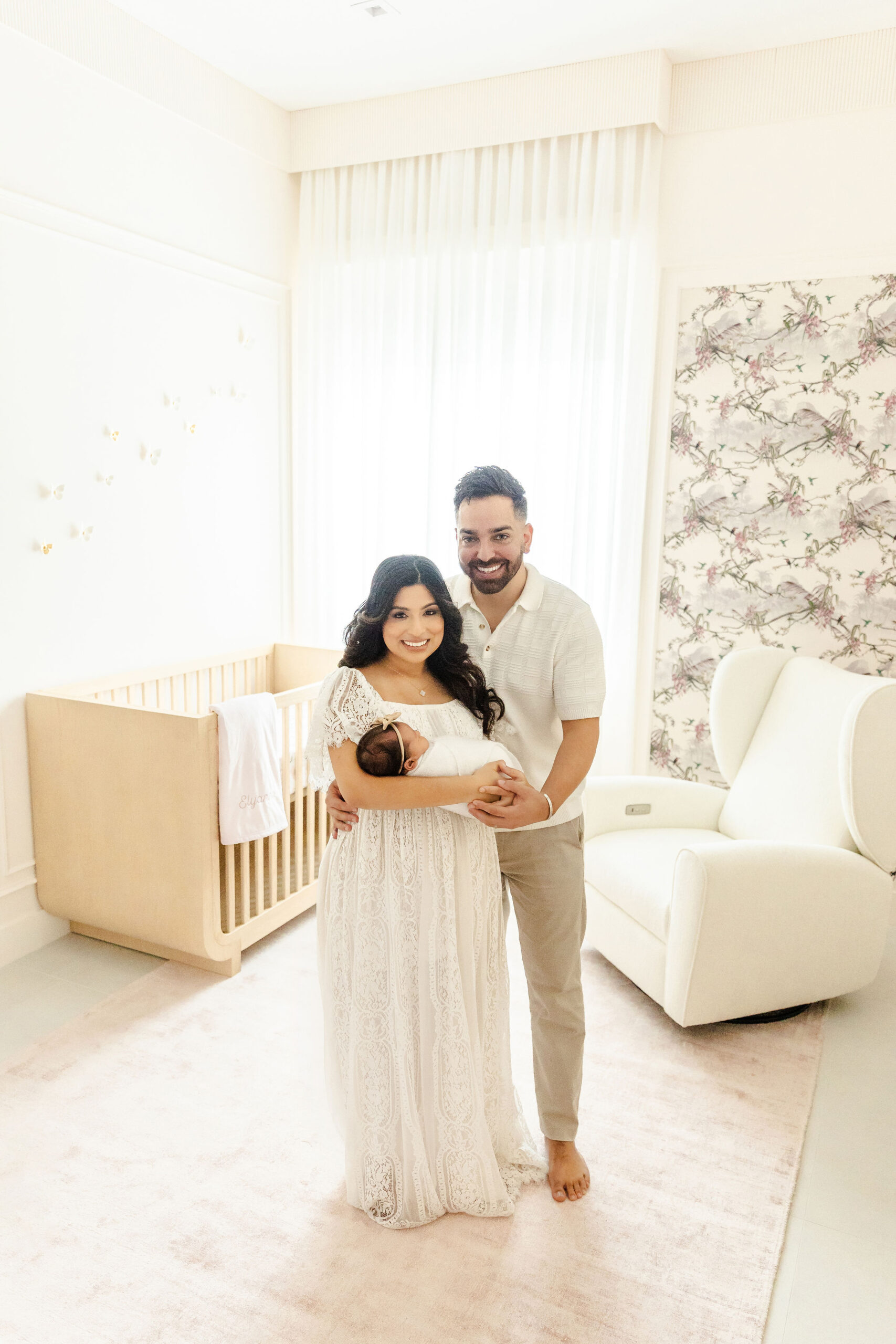 Smiling new mom and dad stand in a nursery holding their sleeping newborn baby girl after meeting lactation consultant in fort lauderdale