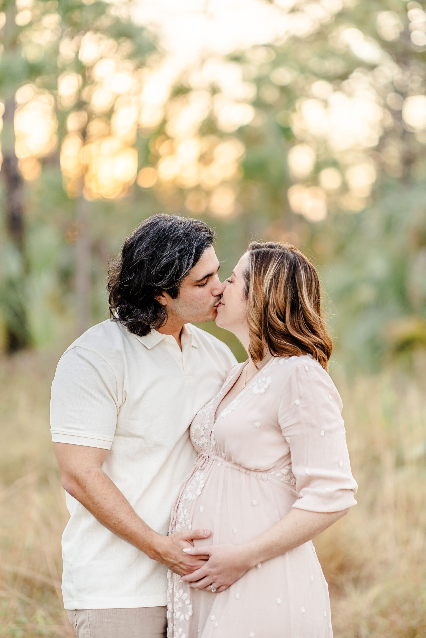 A pregnant couple kisses at sunset in a field with hands on the bump after a prenatal massage in fort lauderdale