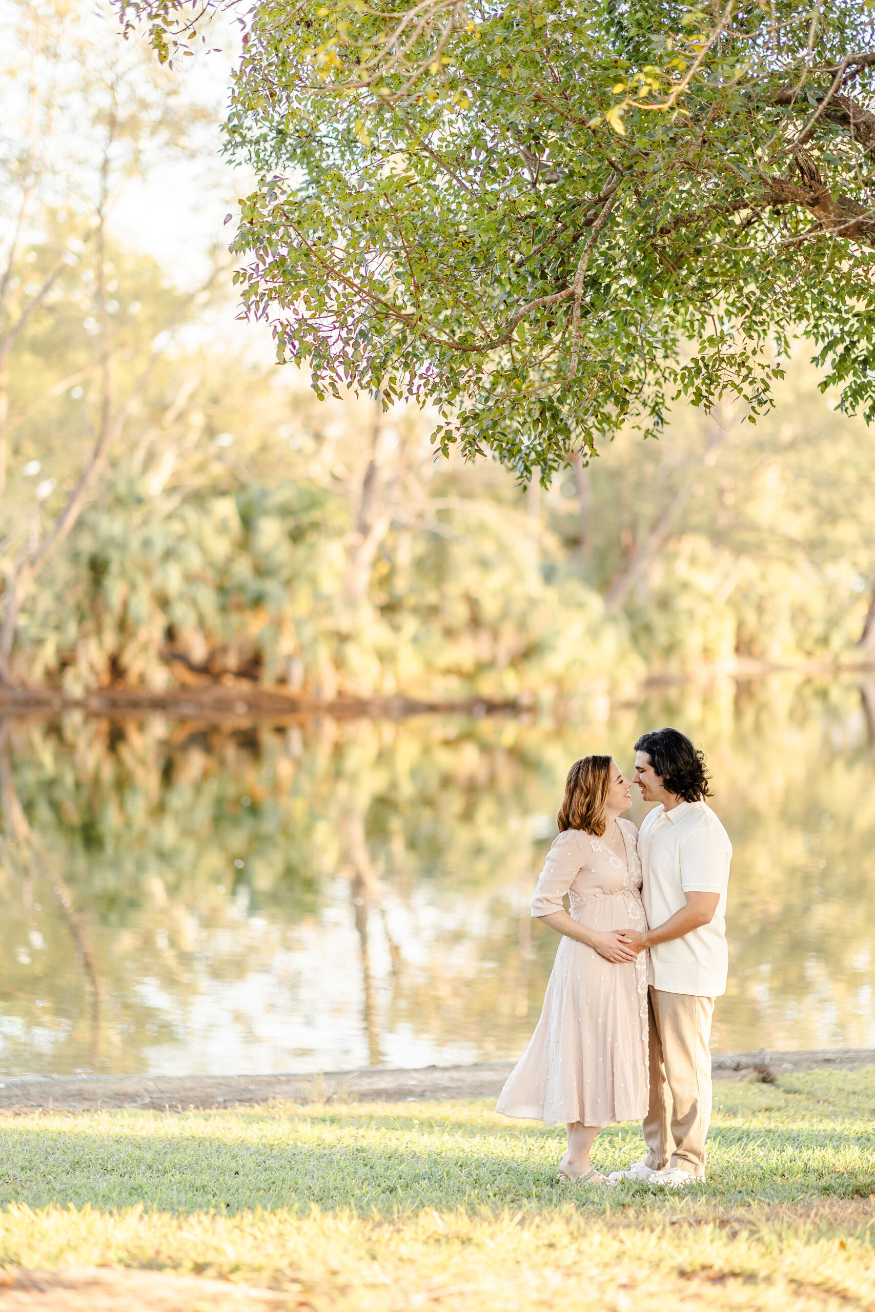 A happy expecting couple lean in for a kiss with hands on the bump on the edge of a lake after a prenatal massage in fort lauderdale