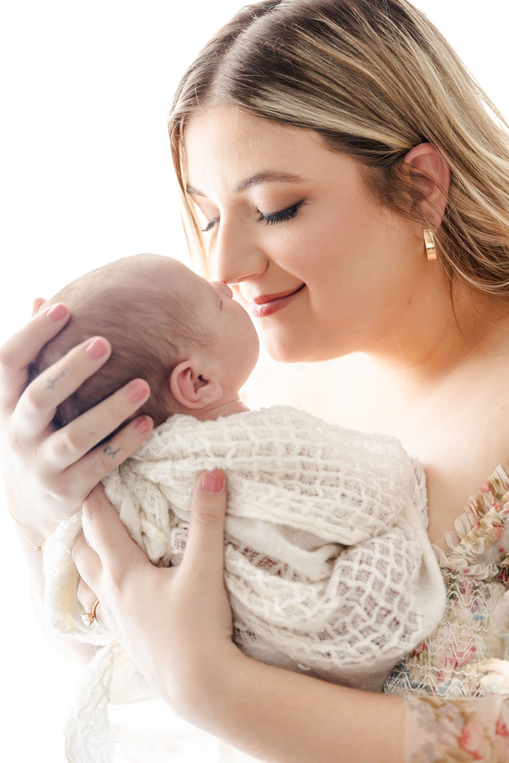 A happy mother boops noses with her sleeping newborn in her hands