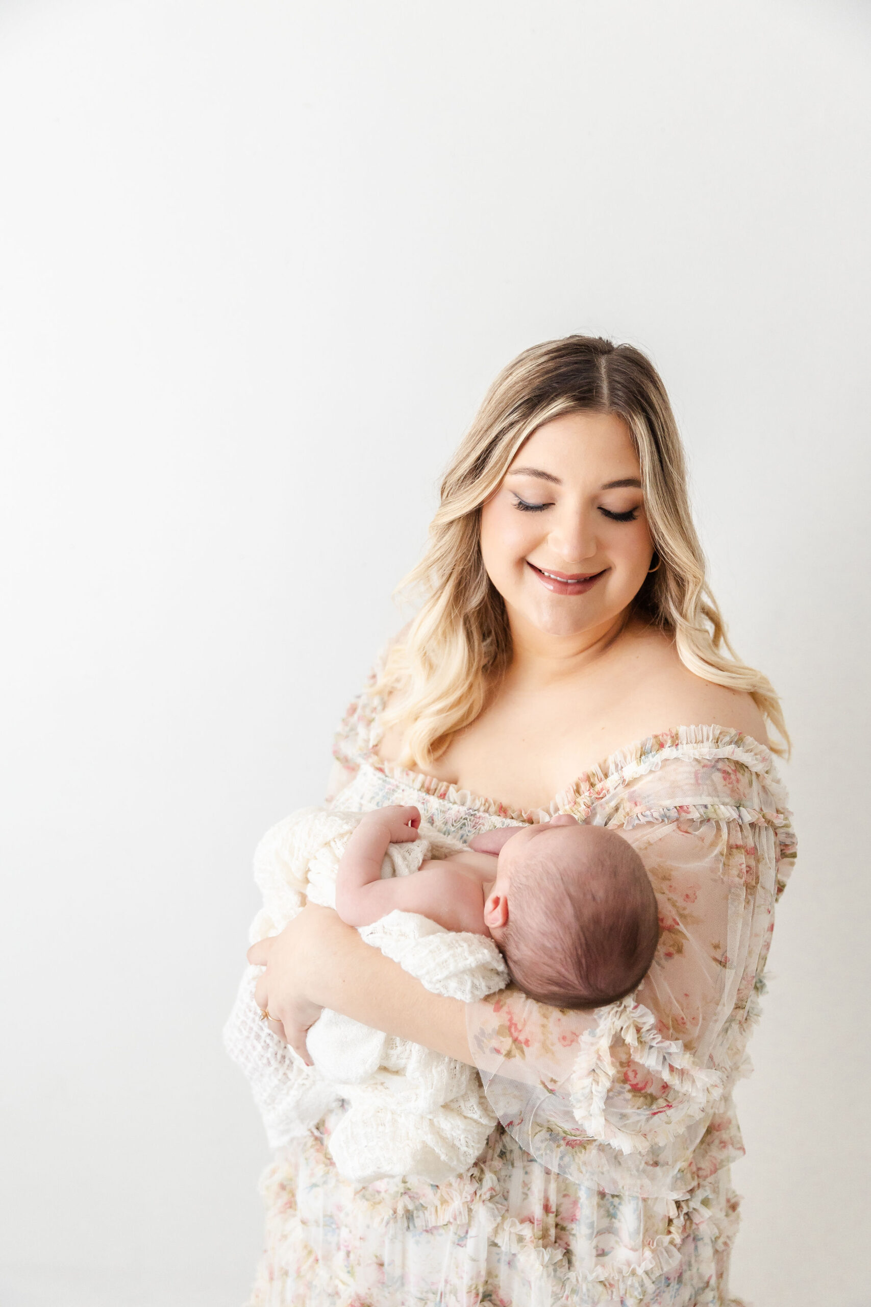 A smiling new mom in a floral print dress smiles down to her newborn in her arms after some pelvic floor therapy in fort lauderdale