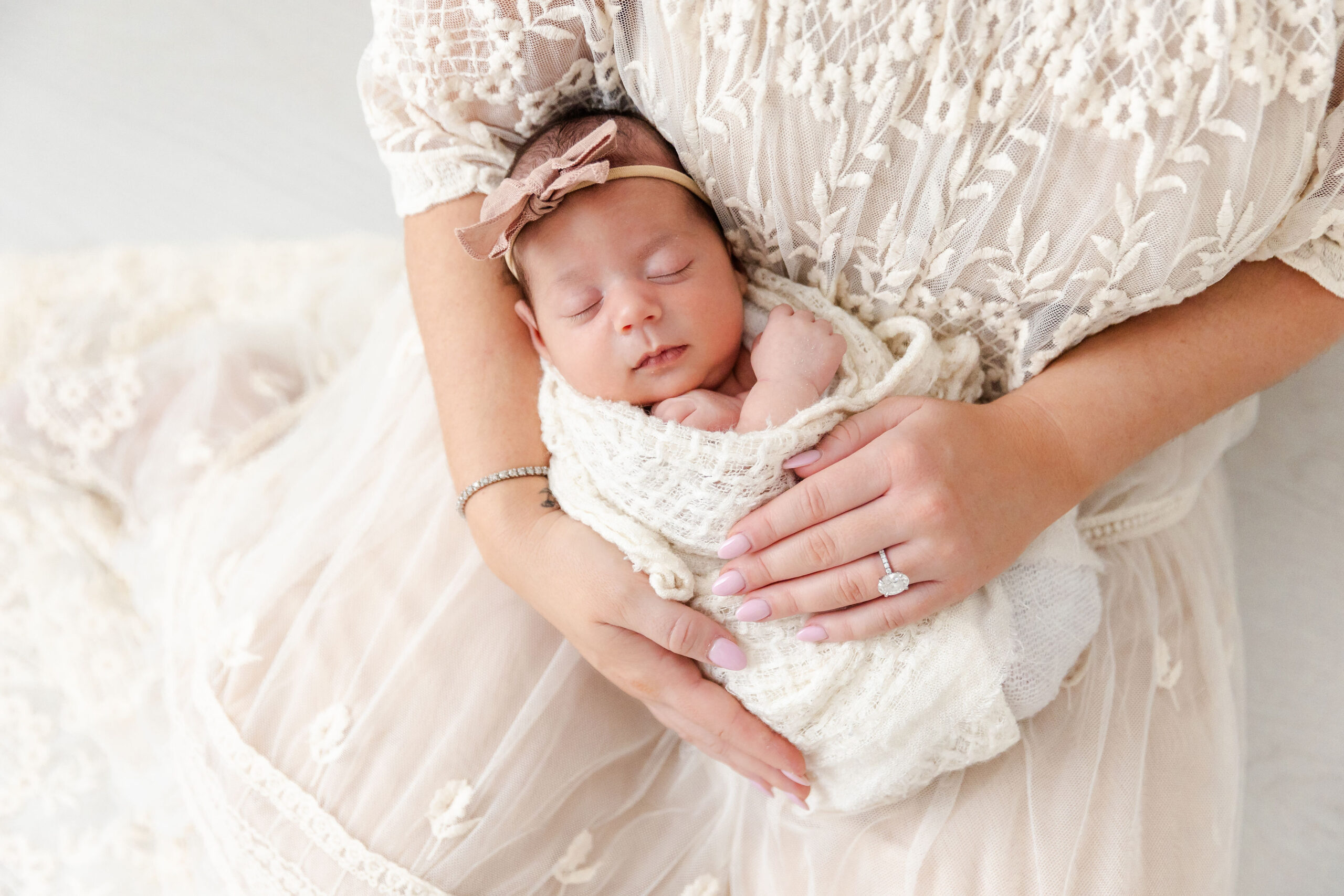 A peaceful sleeping newborn baby girl in a white swaddle in mom's lap on a bed