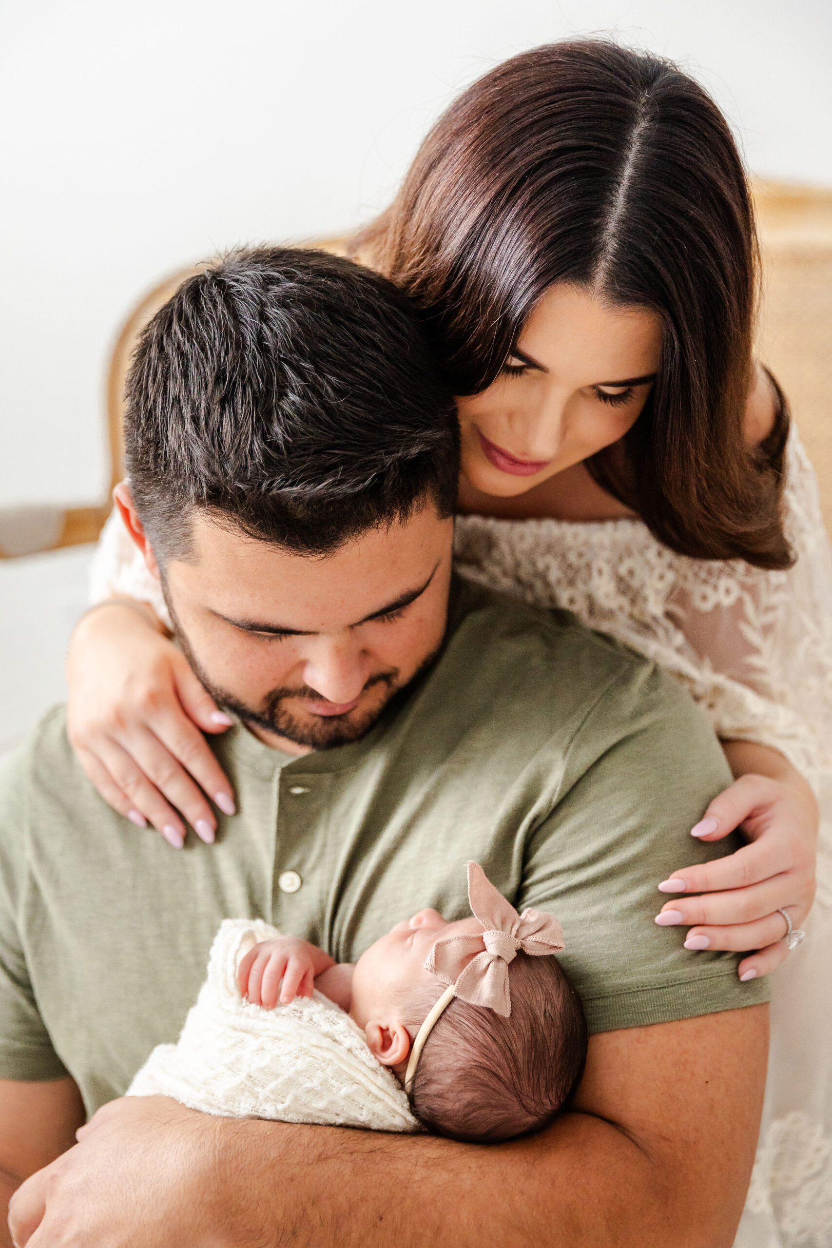 New parents admire their sleeping newborn daughter in dad's arms while sitting on a bed before some infant swim lessons in fort lauderdale