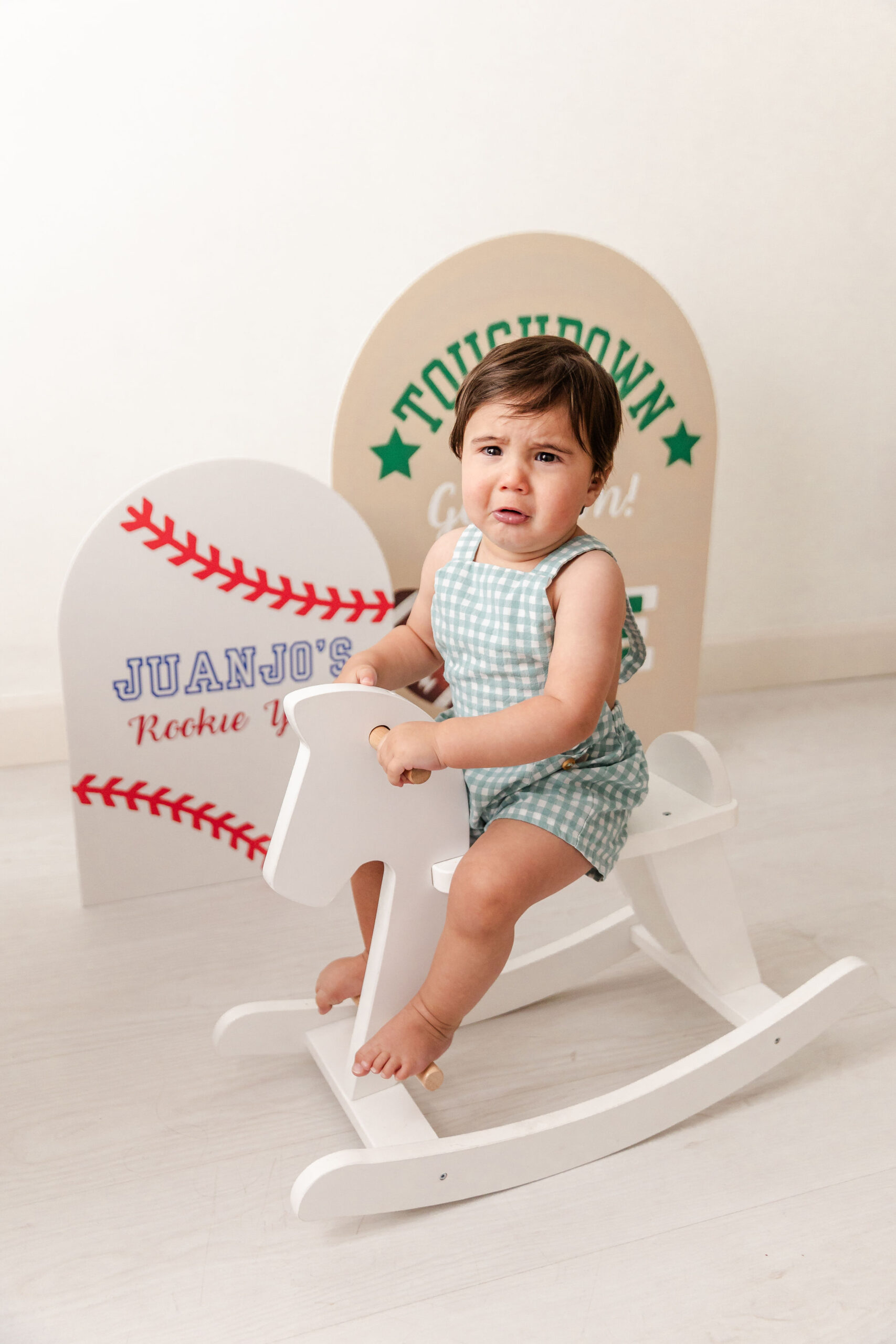 An infant cries while sitting on a wooden rocking horse in a studio before visiting toy stores in fort lauderdale