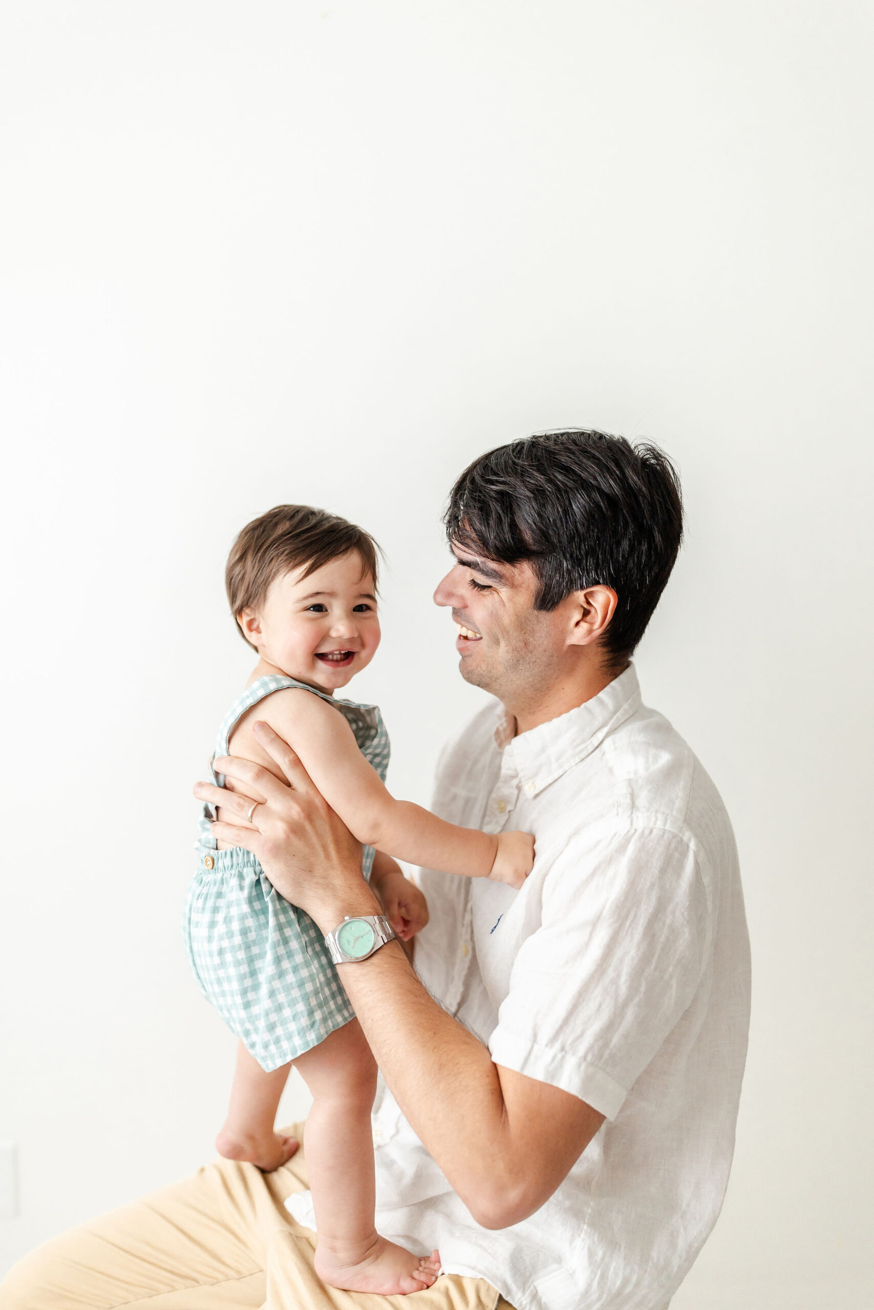 A happy new dad sits and plays with his toddler standing in his lap