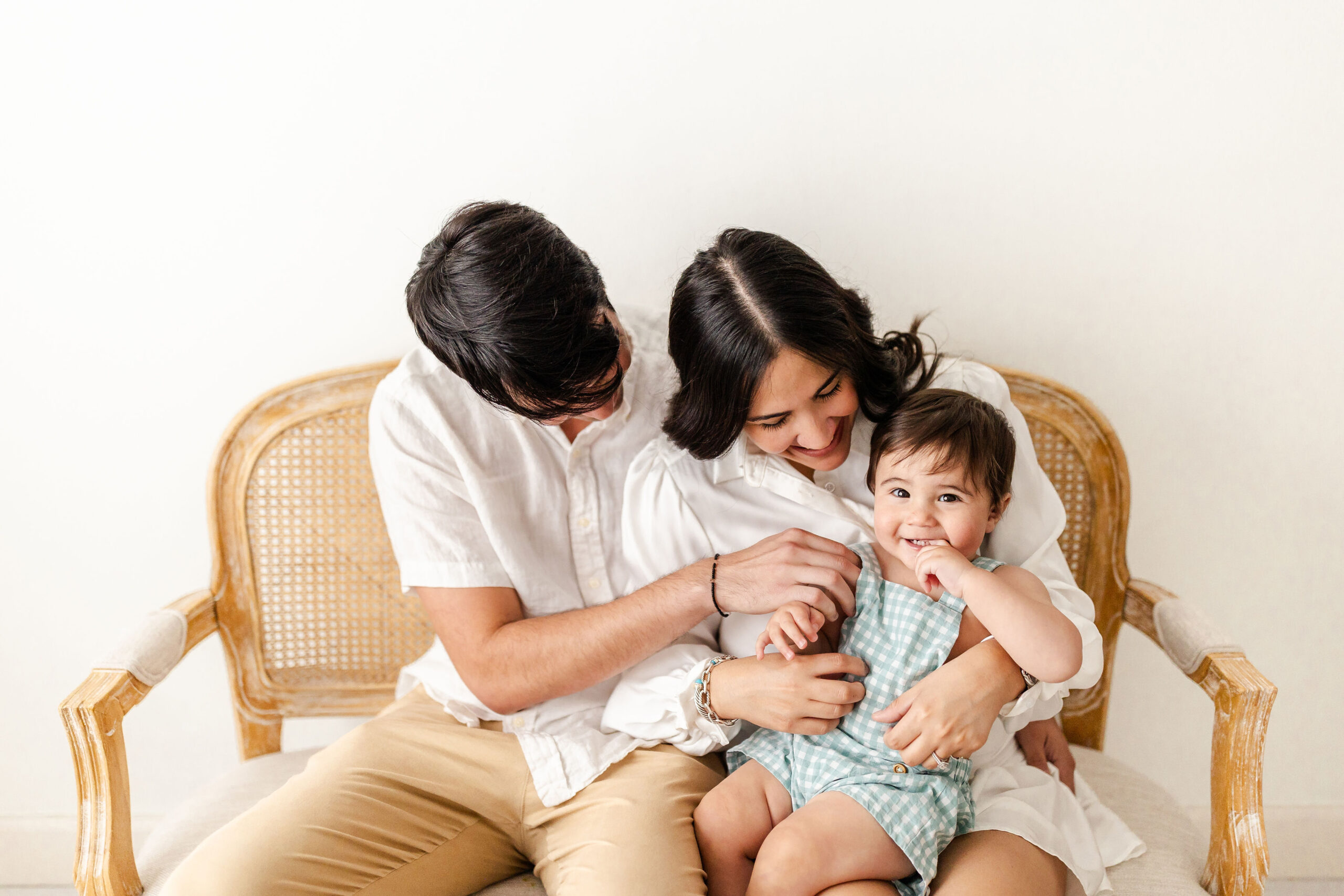 A happy infant sits in mom and dad's laps on a bench as they tickle him before visiting indoor playgrounds in fort lauderdale