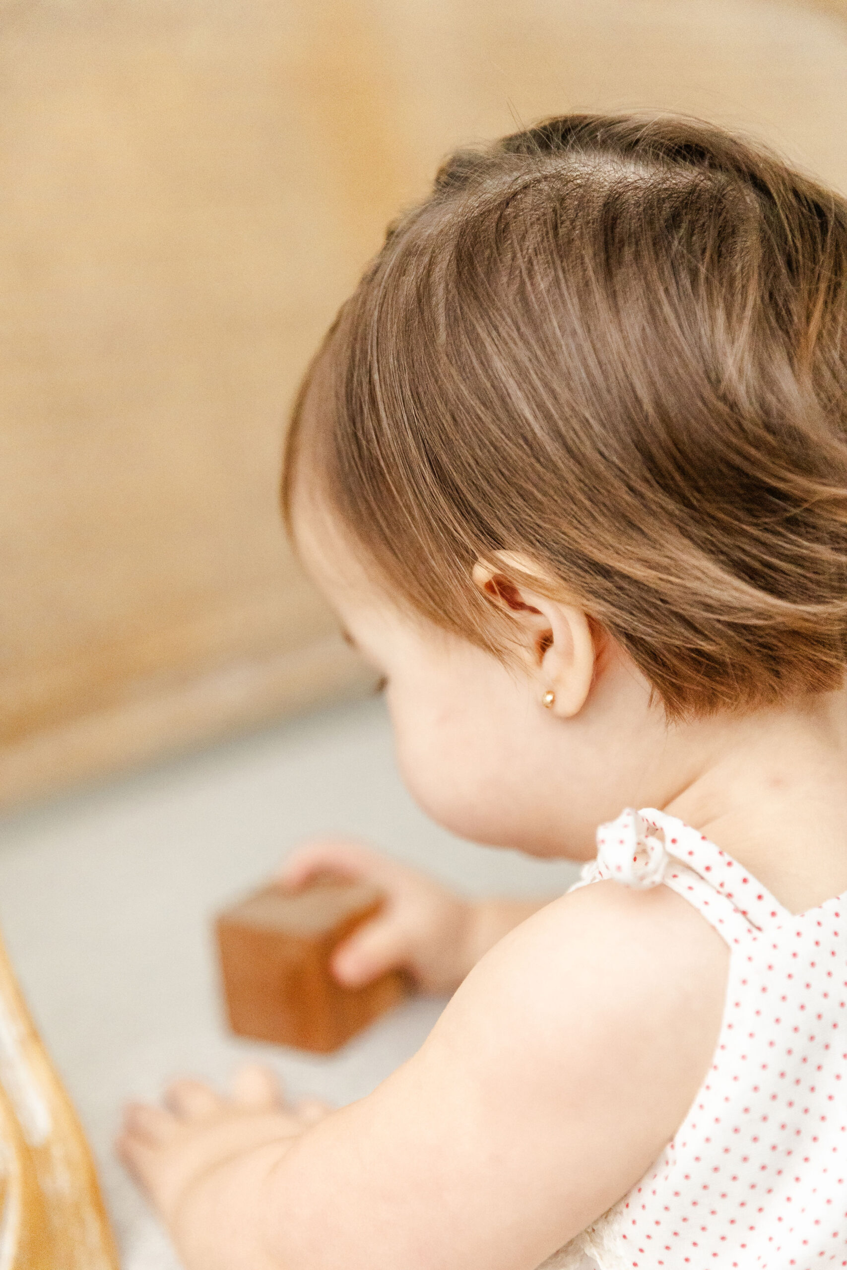 A look over the shoulder of a baby in a white dress playing with wooden blocks during some toddler activities in fort lauderdale