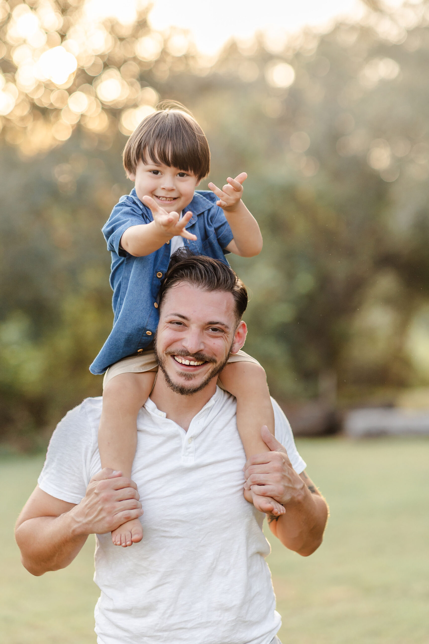 A toddler boy in a denim shirt plays spiderman while sitting on dad's shoulders in a park while staying at kid friendly hotels in fort lauderdale