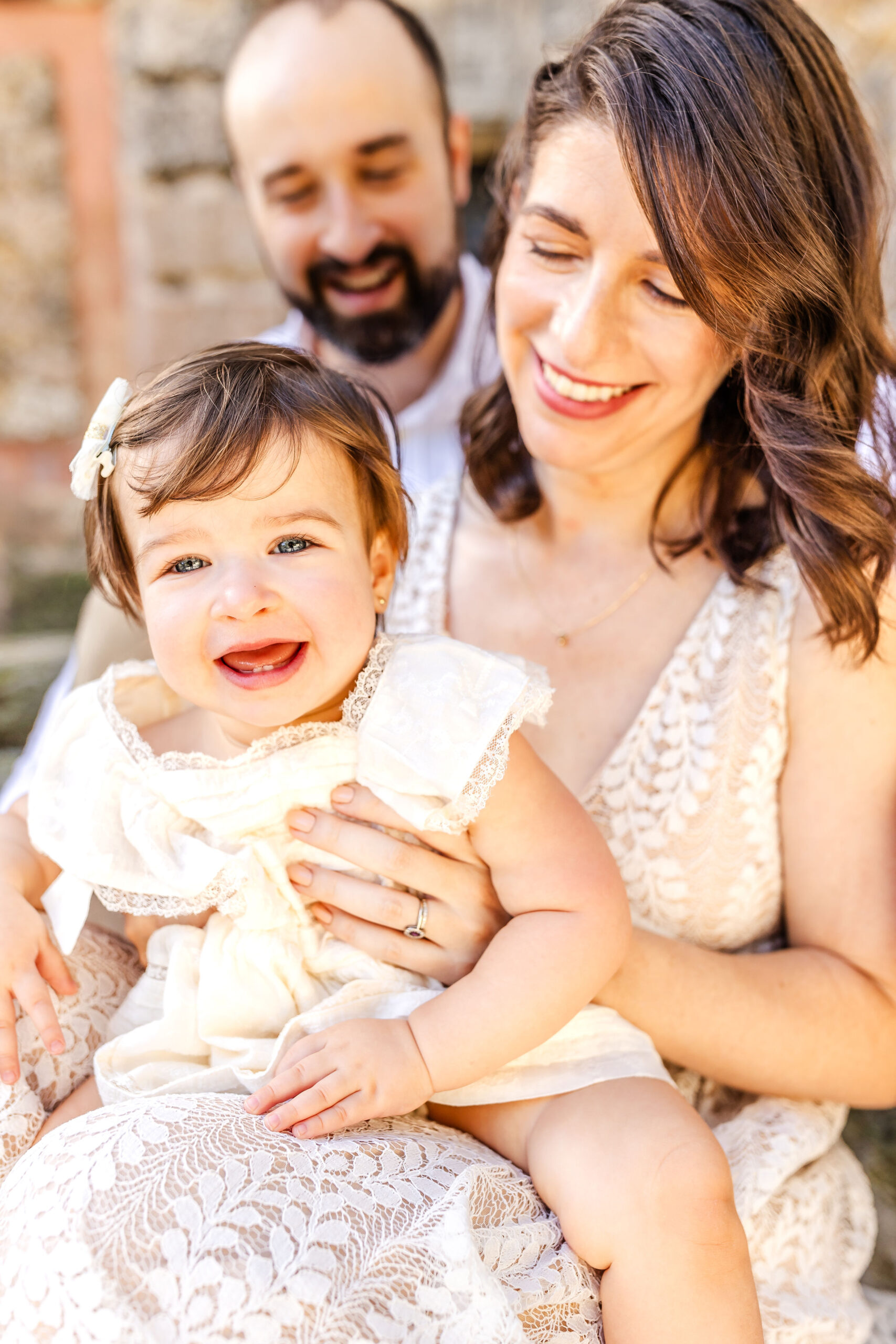 A young infant girl sits on moms lap laughing in a white dress before visiting kid friendly restaurants in fort lauderdale
