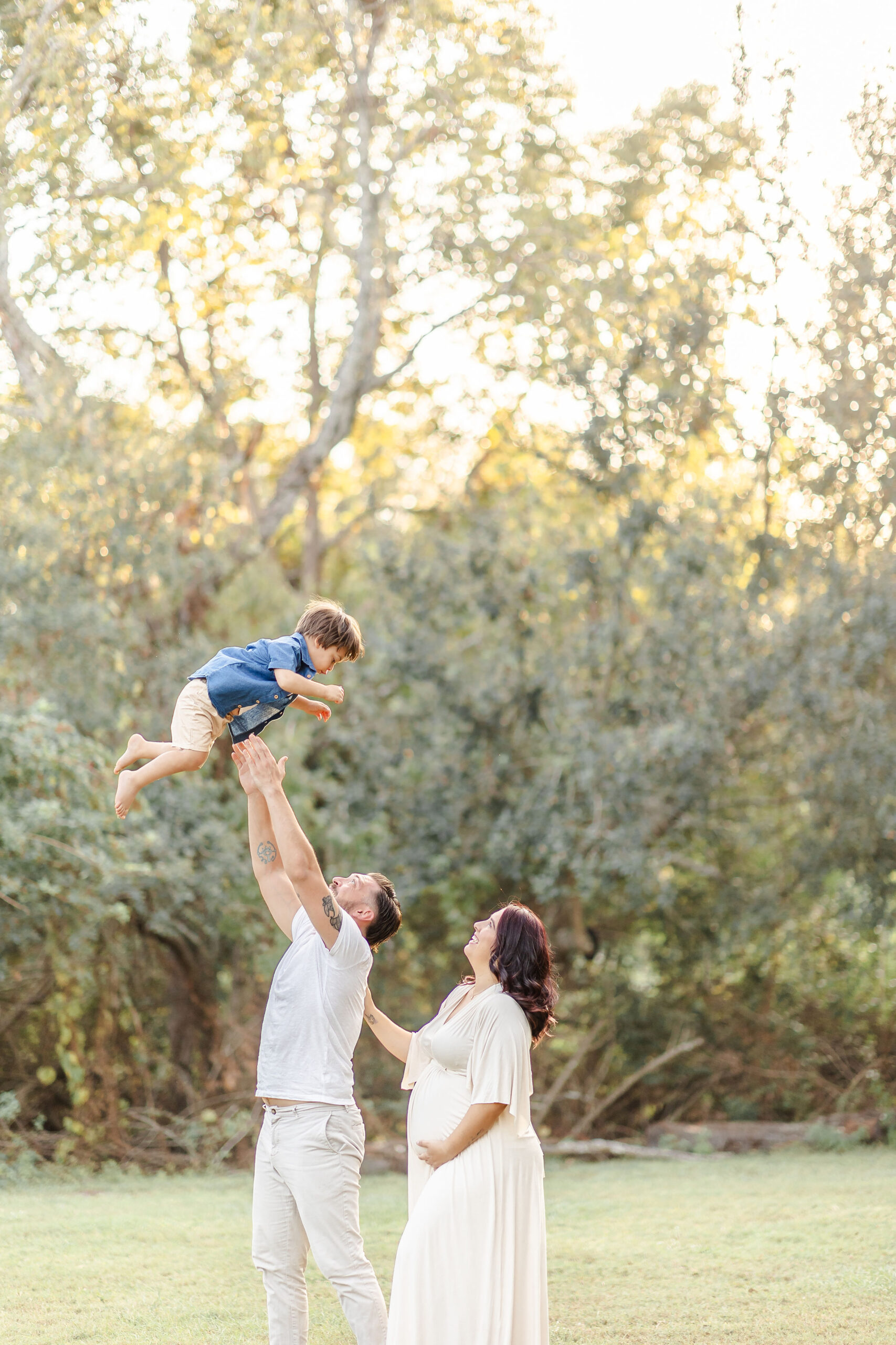 A happy mom and dad in a park at sunset tossing their happy son above their heads in a denim shirt
