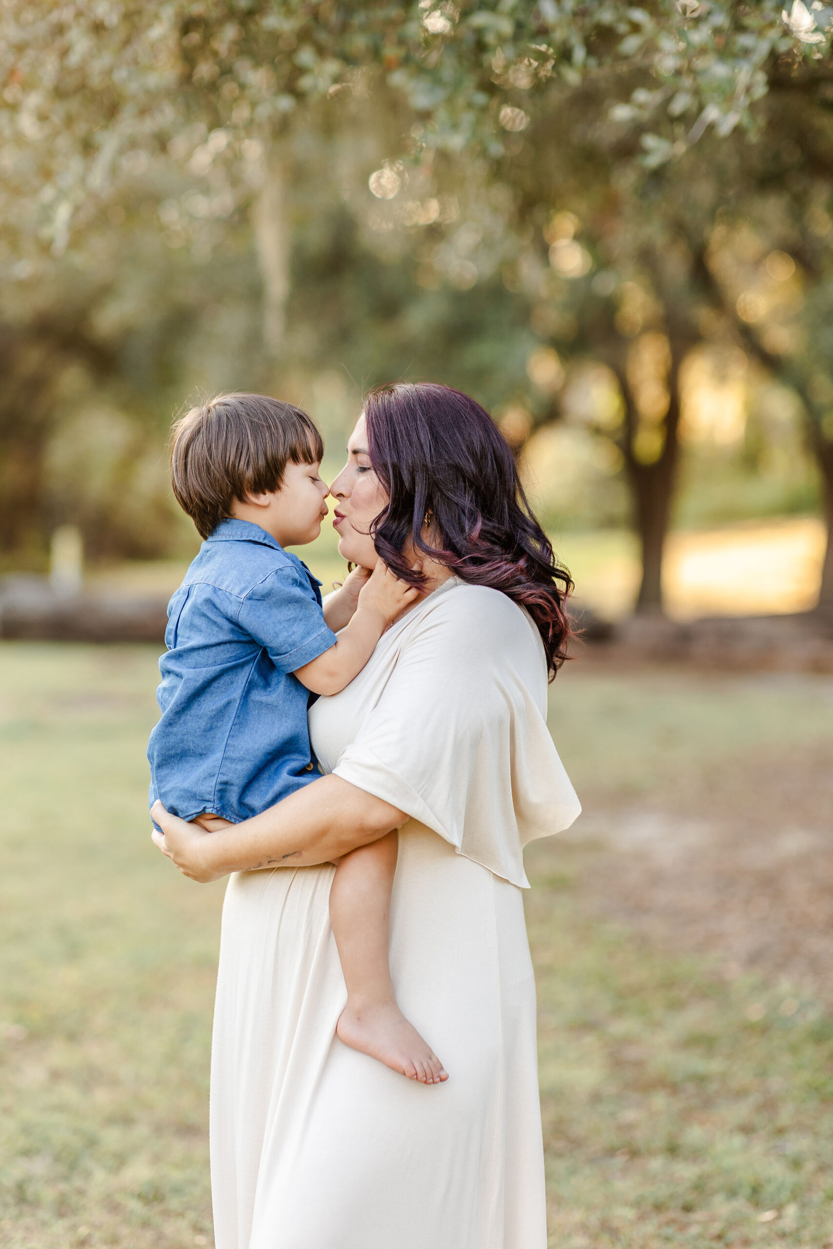 A happy mom in a white dress kisses her toddler sitting in her hands in a park before visiting fall festivals in fort lauderdale