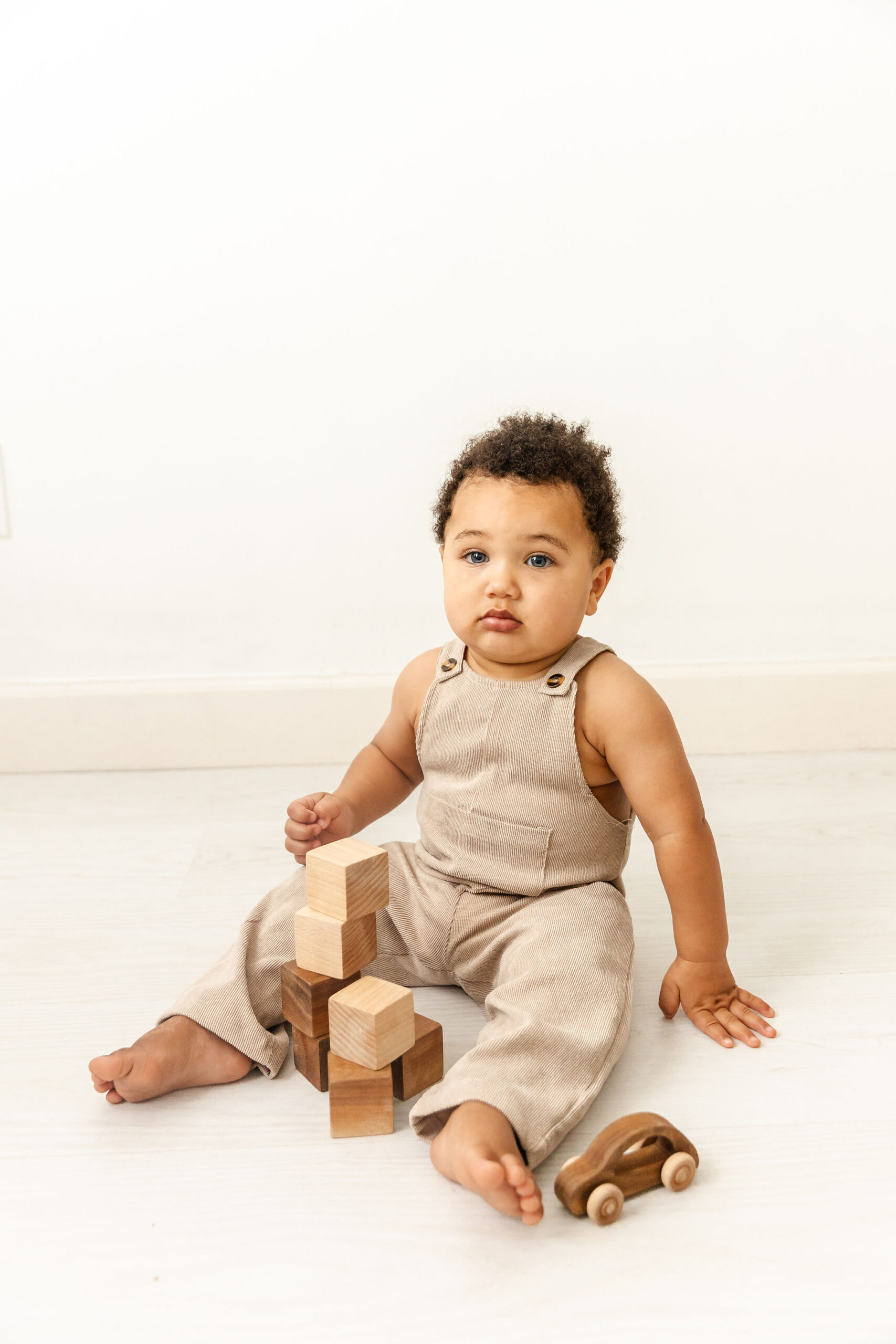 An infant in tan overalls sits on the floor of a studio playing with wooden blocks before visiting fort lauderdale childrens museums