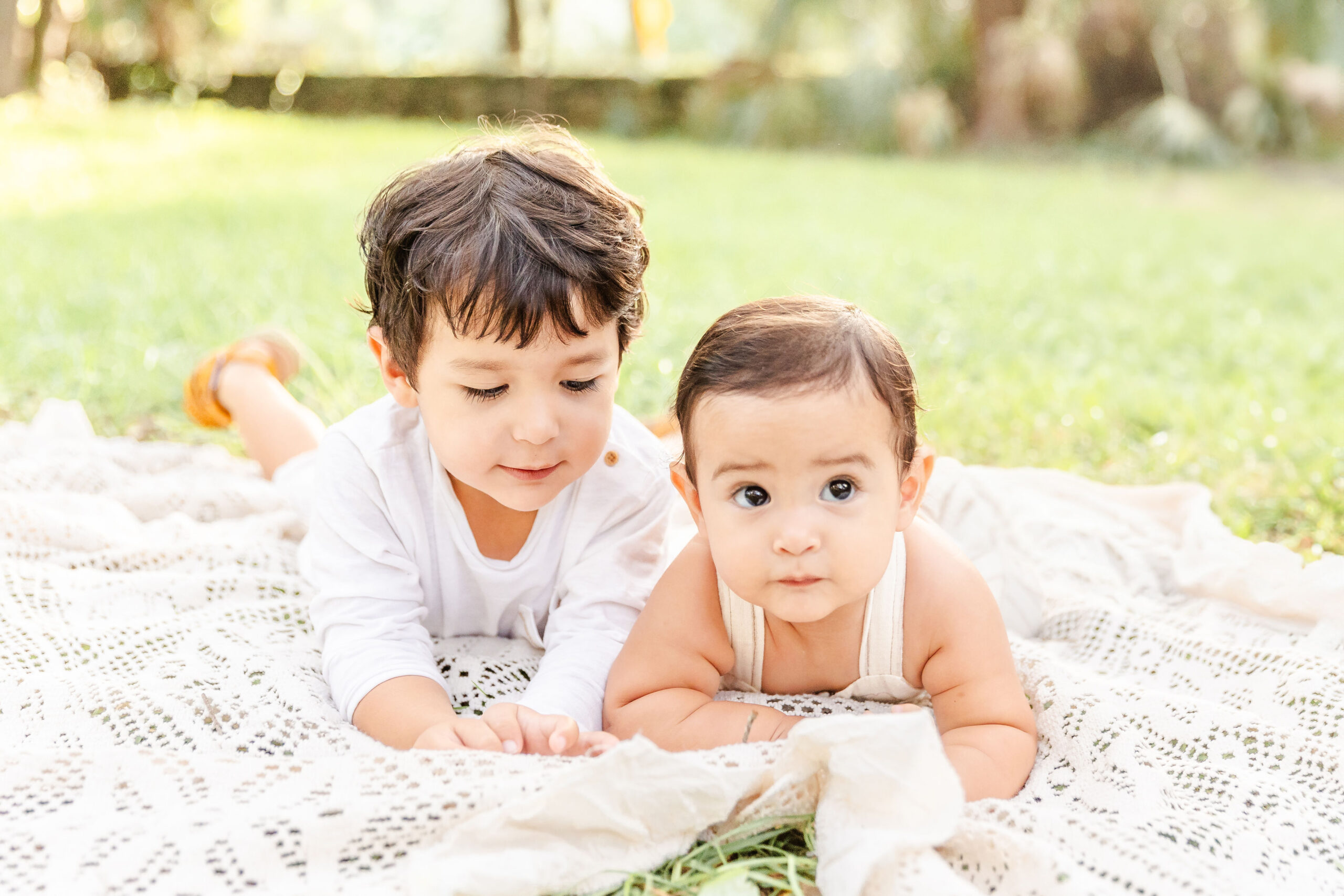 Toddler brothers lay on a picnic blanket in a park in white outfits after visiting pediatric chiropractors in fort lauderdale