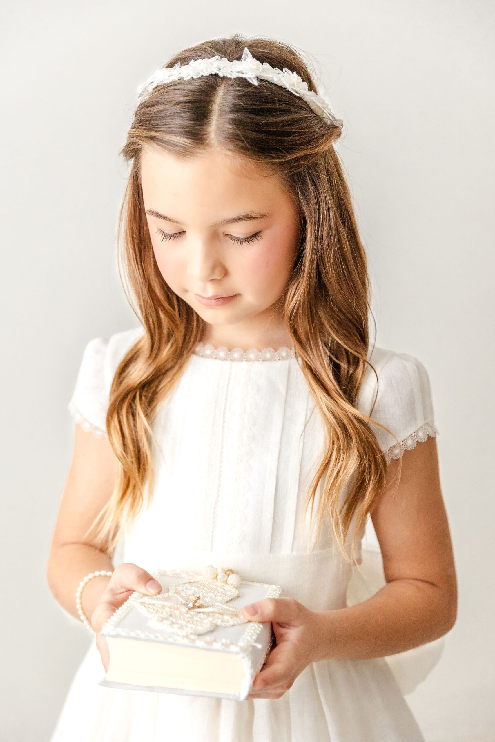A young girl in white smiles down to a pearl covered bible in her hands after finding first communion dresses in miami