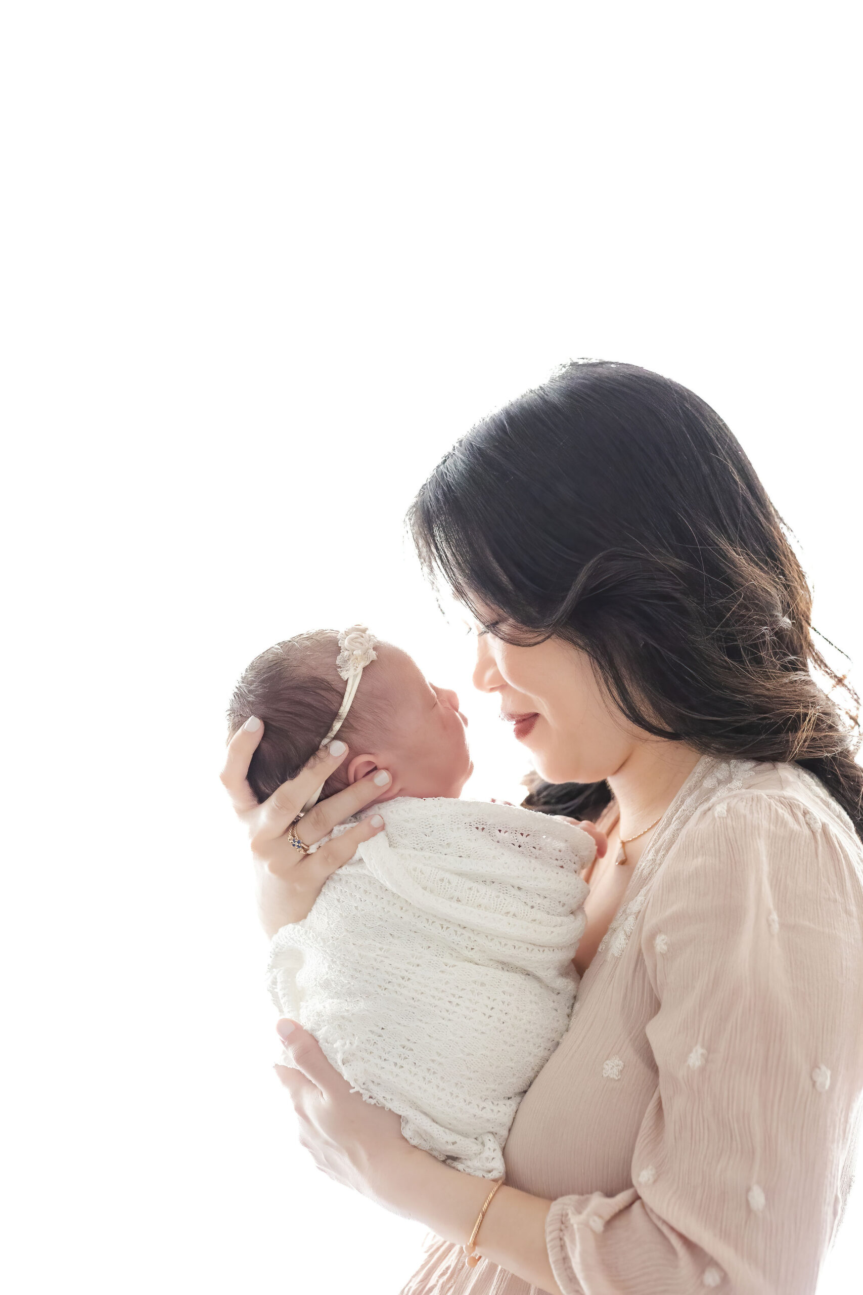 A happy new mom boops noses with her sleeping newborn against her chest in a white swaddle after visiting Baby stores in coral gables