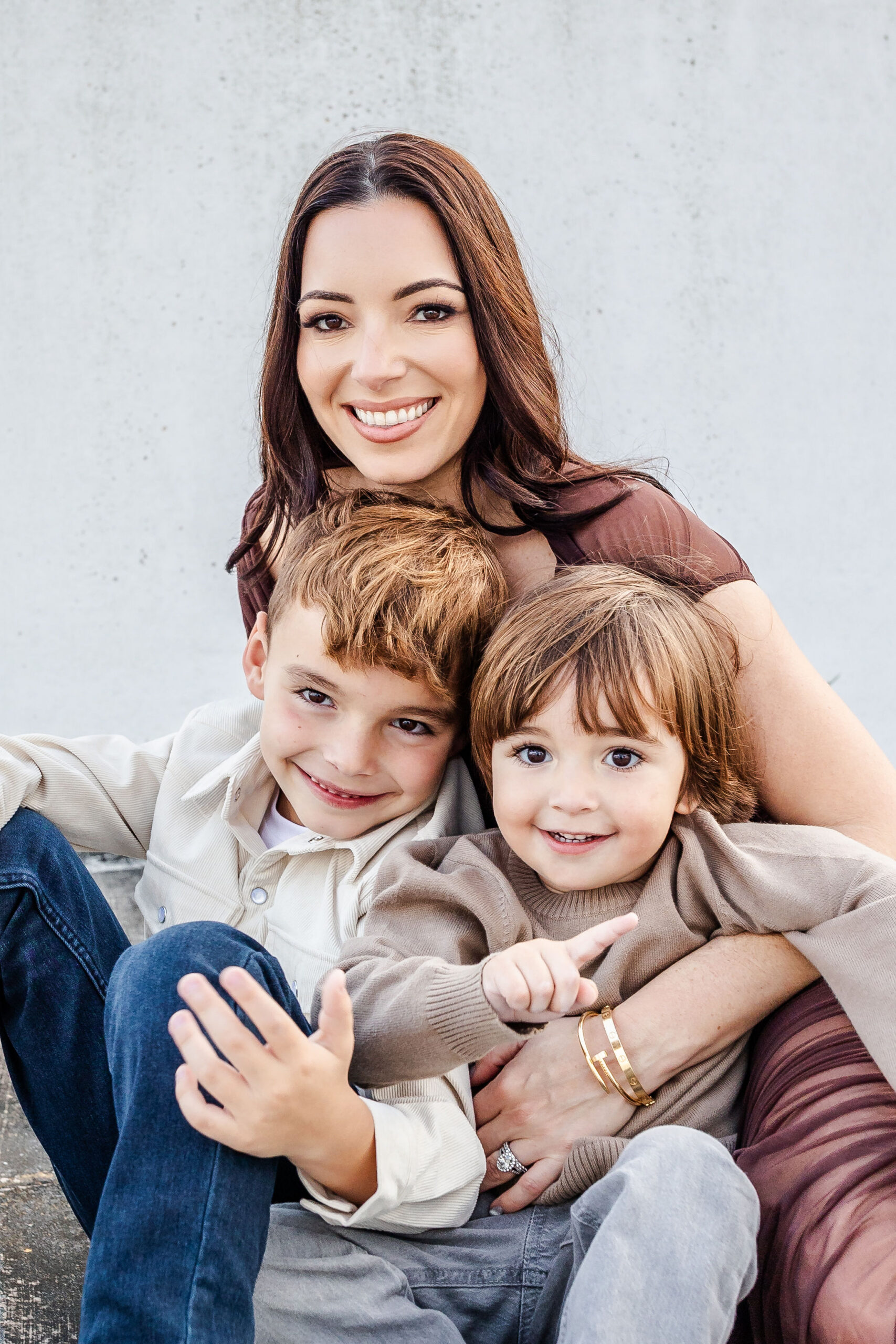 A happy mother in a brown dress sits with her two toddler sons smiling after visiting pediatric dentists in coral gables