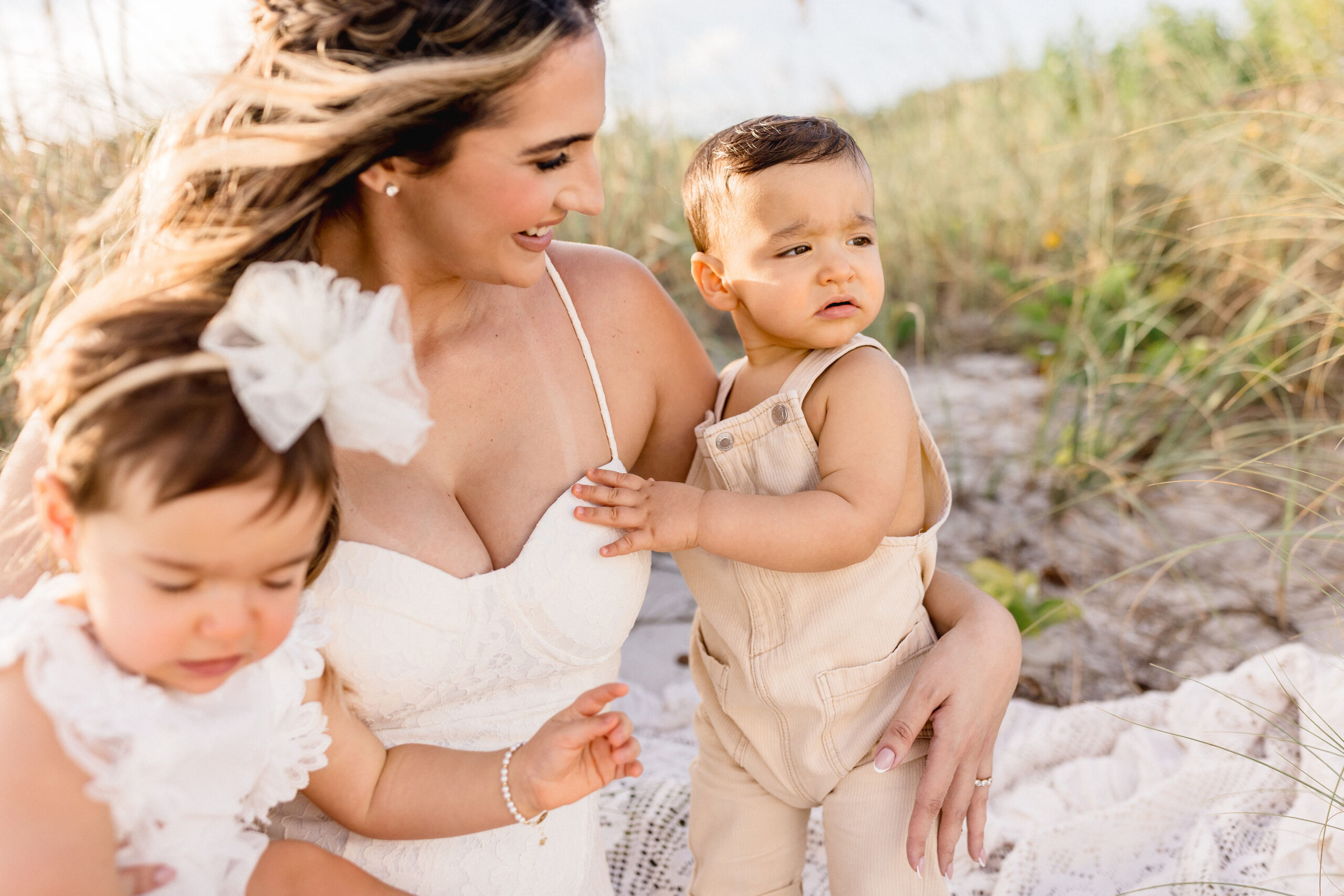 A toddler boy and girl experience a windy beach with happy mom in white at sunset after some mommy and me classes in coral gables