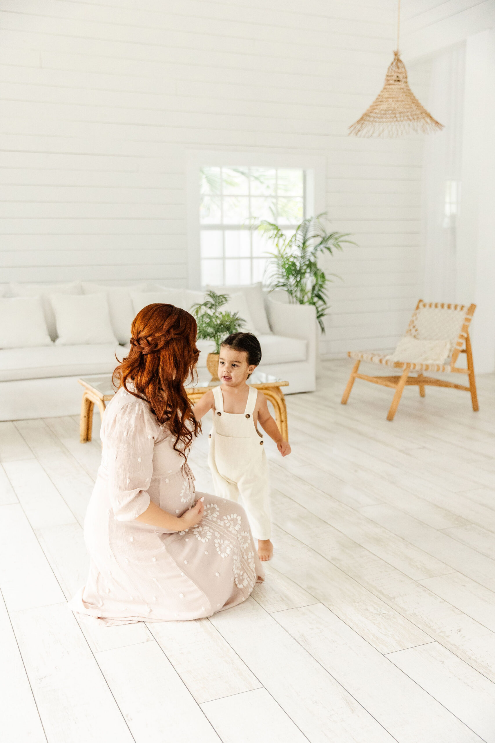 A pregnant mother plays with her toddler son in a white room