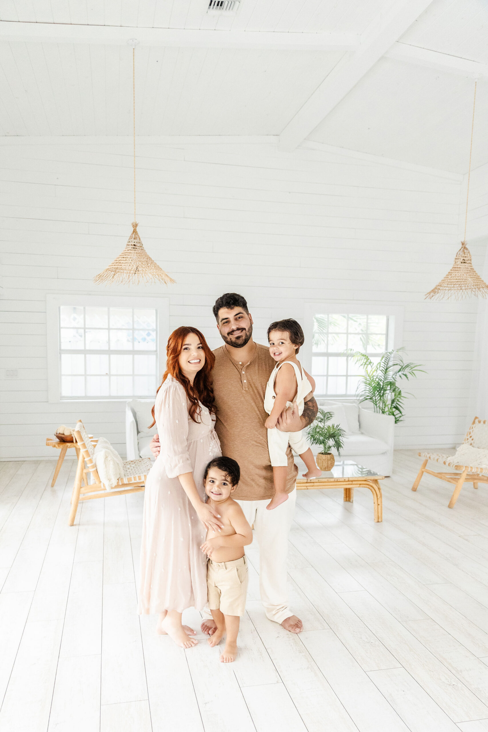 Happy mom and dad stand in a studio with their two toddler sons in tan and white after some pelvic floor therapy in coral gables