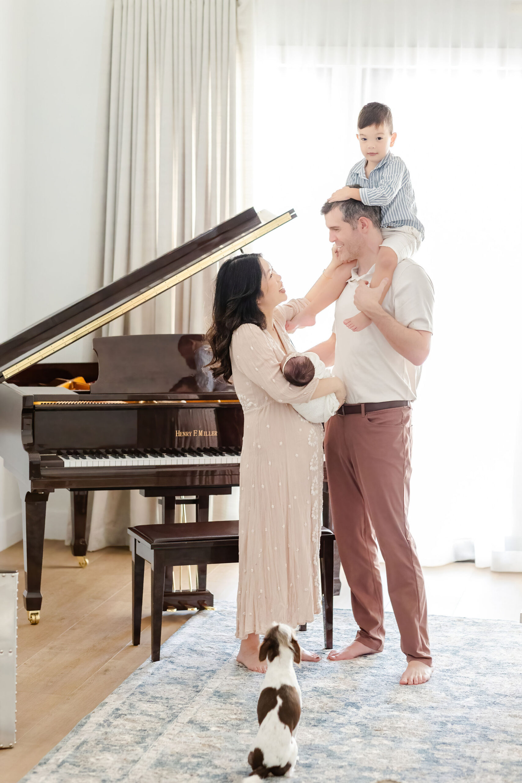 A mom and dad stand by the piano holding a newborn and toddler on dad's shoulders after visiting the wander shop