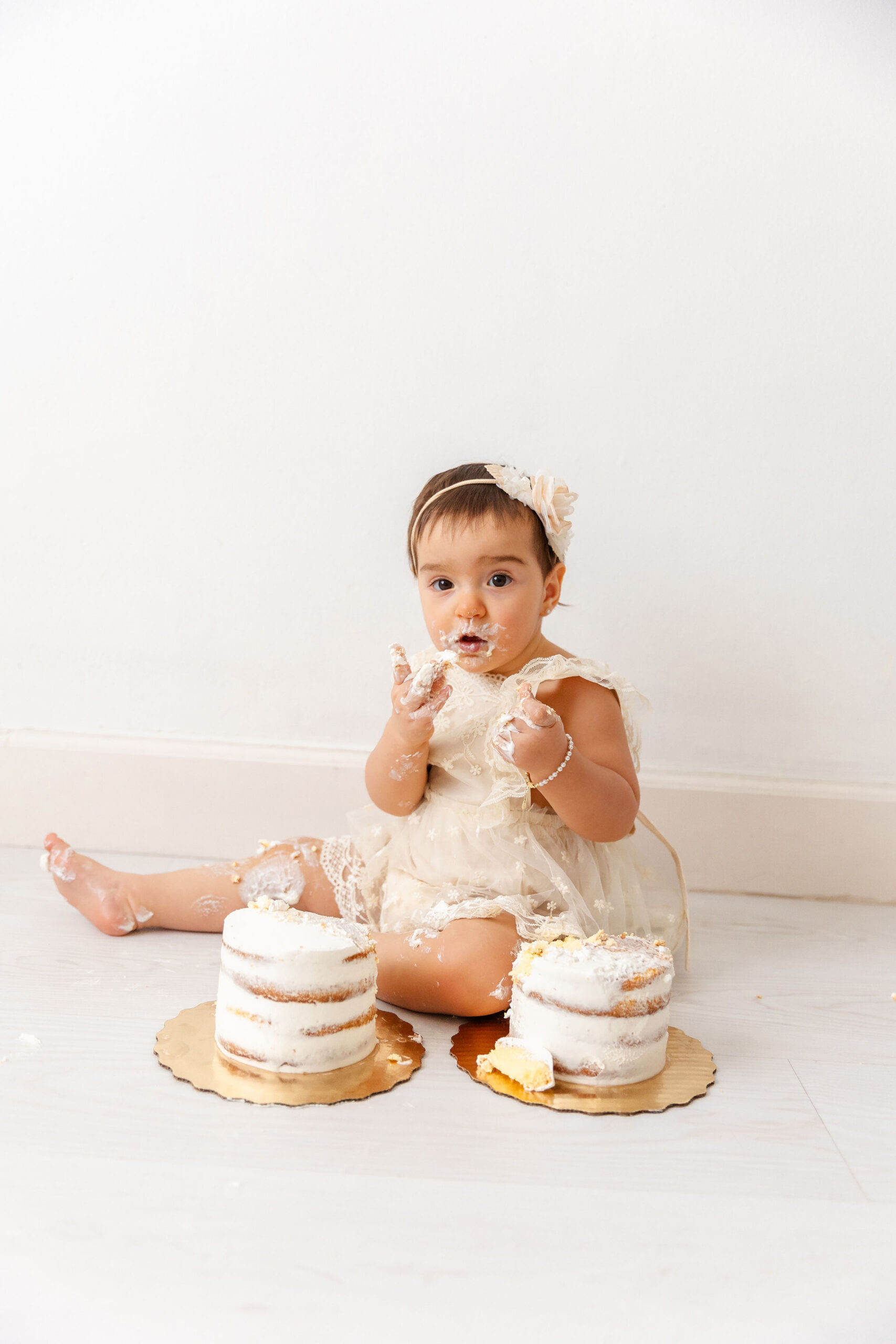 A baby girl in a white dress covered in icing smashes cakes on a studio floor after loving indoor playgrounds in coral gables