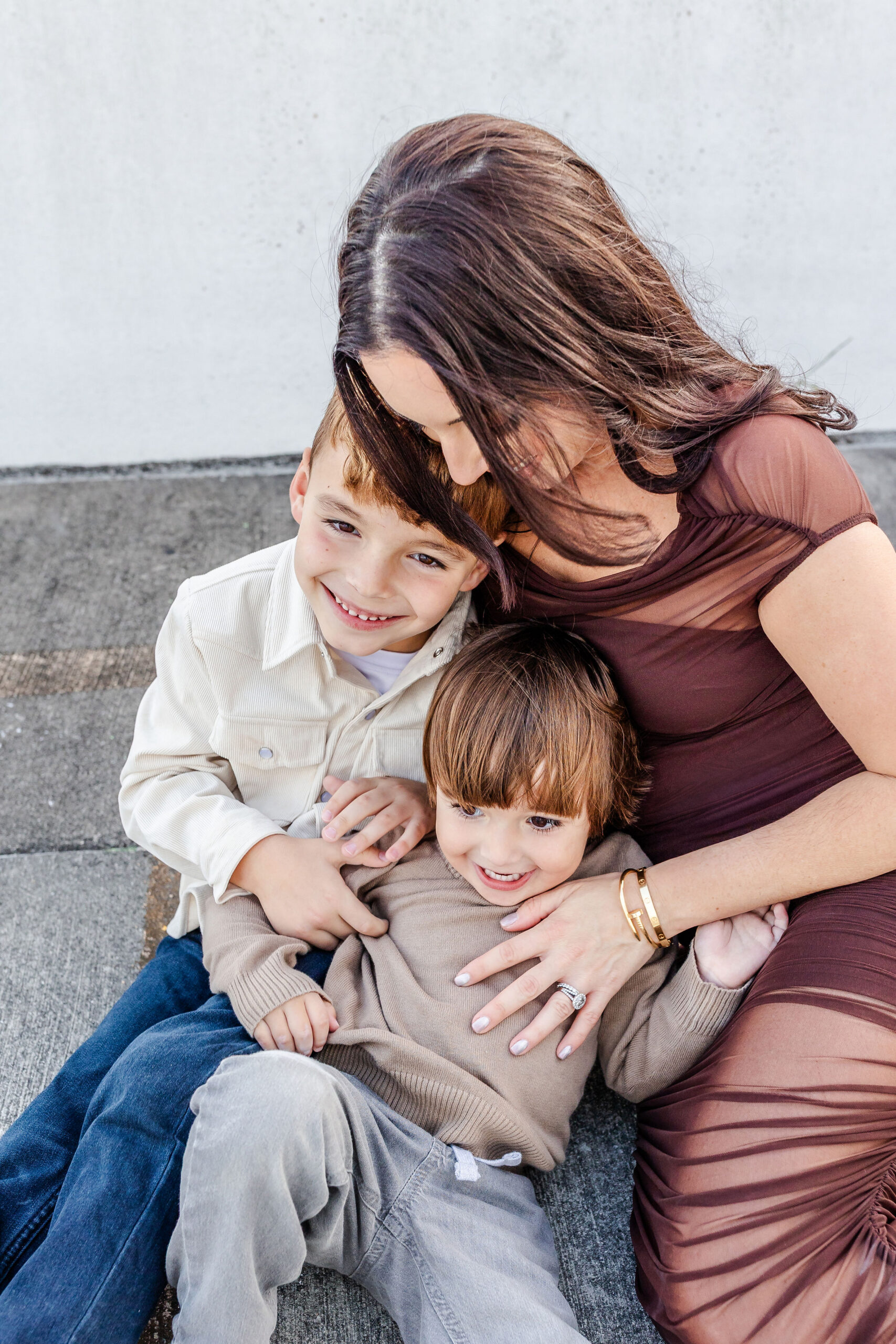 A happy mother in a brown dress snuggles her two toddler sons on a windy day after exploring preschools in coral gables