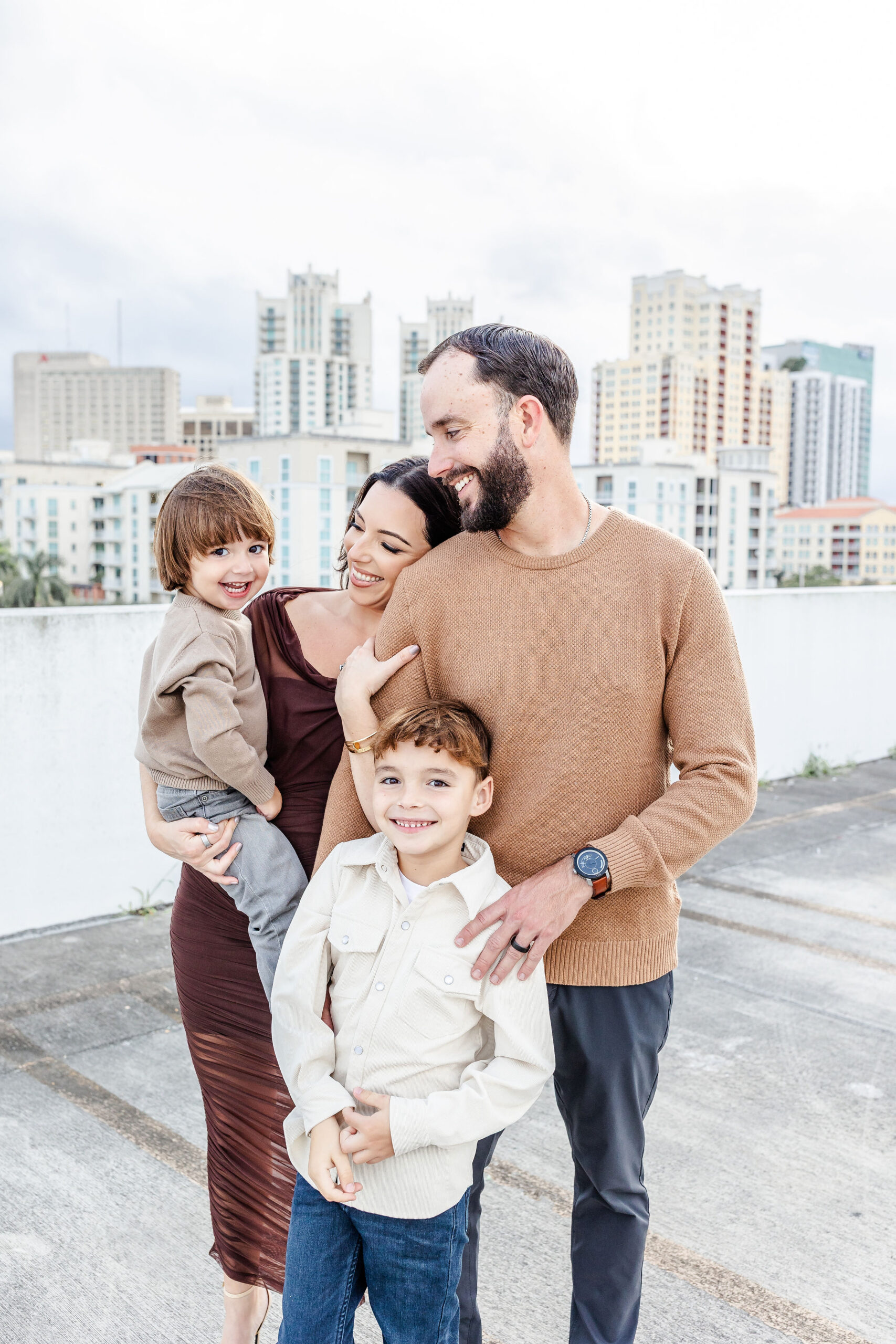 A happy mom and dad laugh while standing on a downtown rooftop after exploring preschools in coral gables
