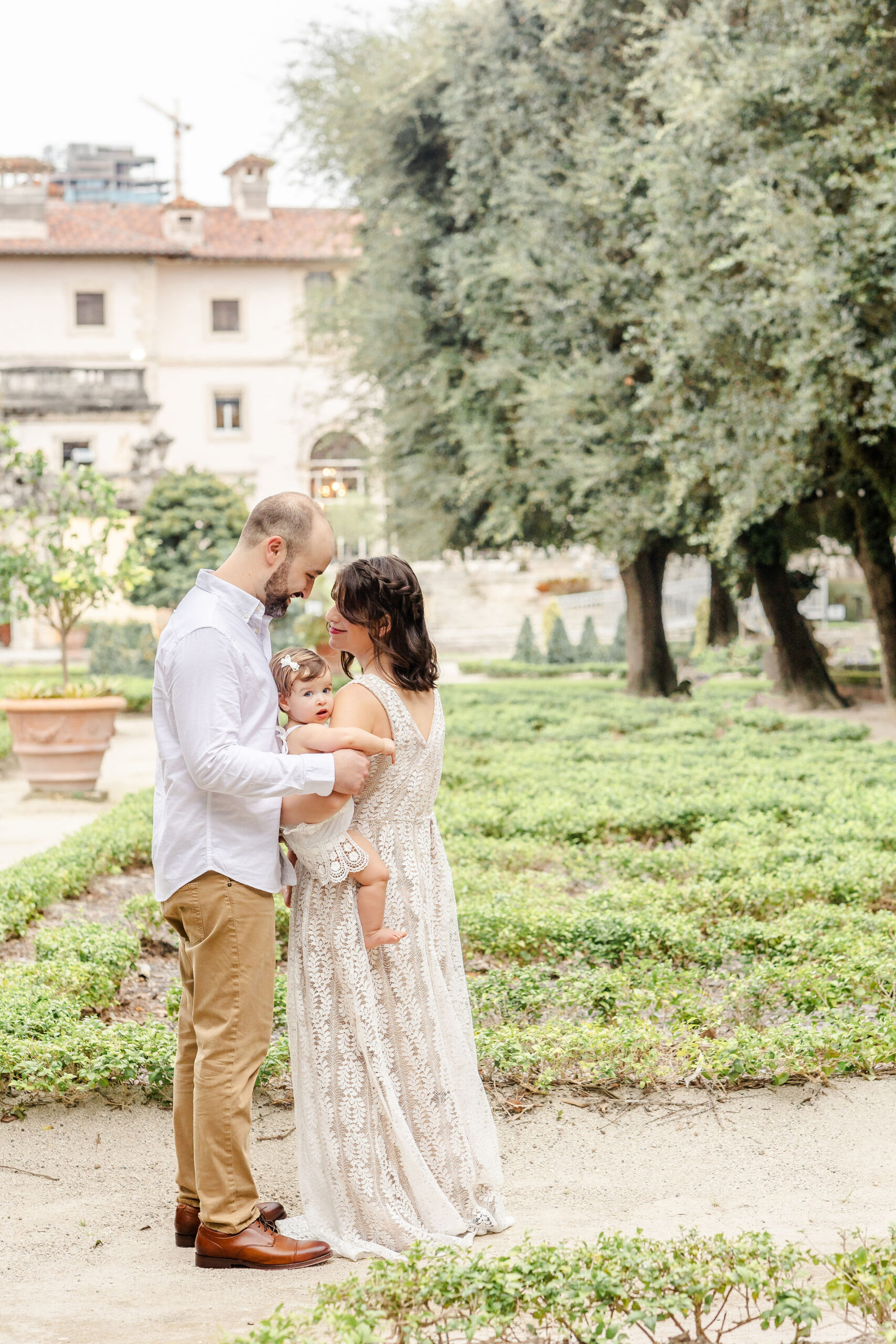 A mom and dad explore a garden in a lace dress and white shirt with their toddler daughter during things to do in coral gables with kids