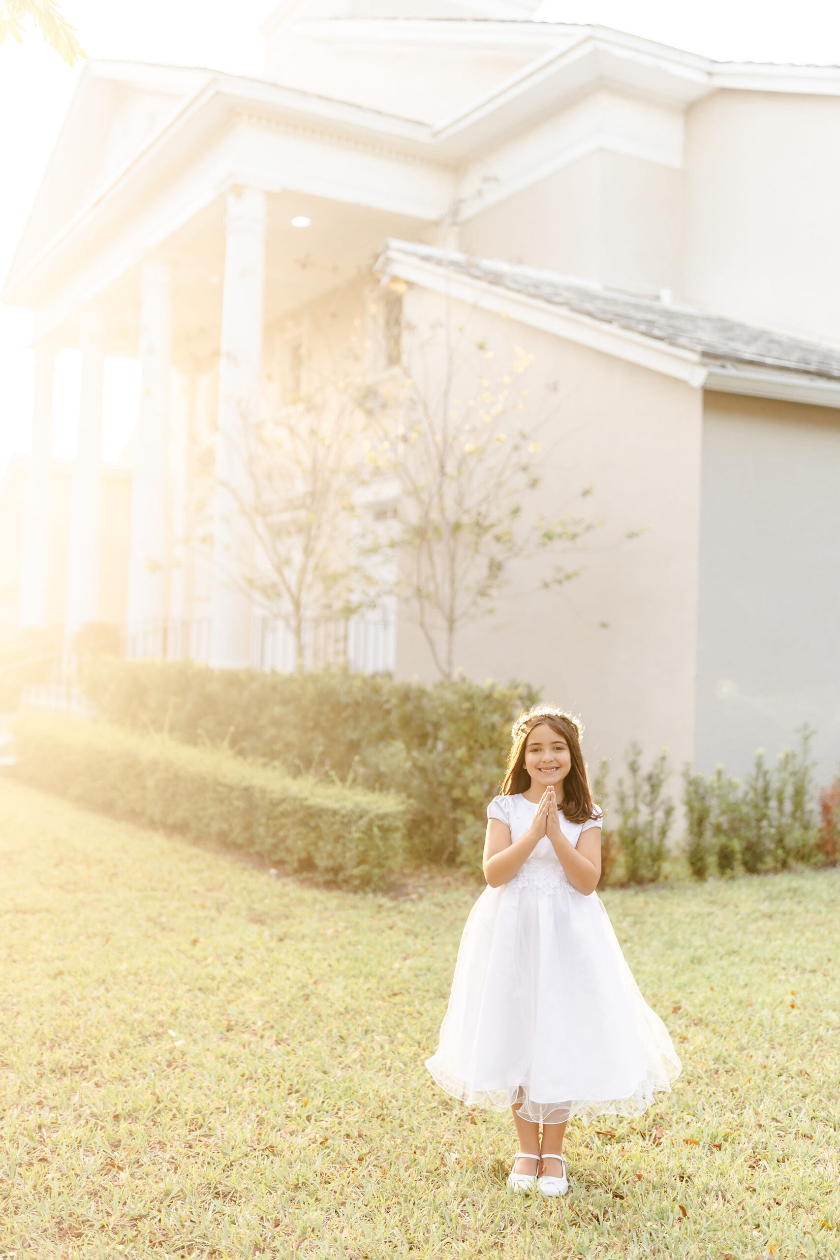 A young girl smiles with hands in prayer while standing in a church lawn at sunrise