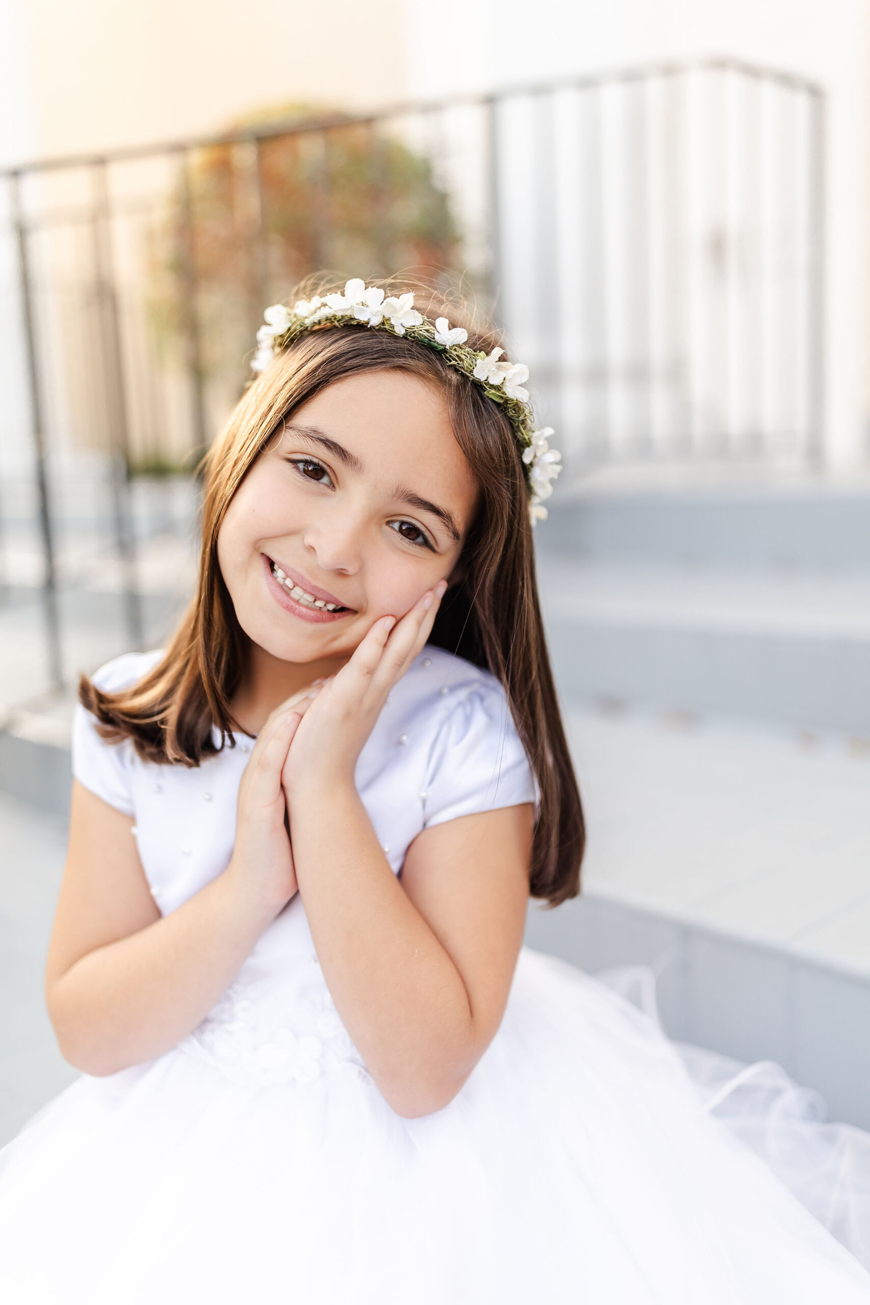 A young girl in a white dress smiles with hands on her cheek on church steps after enjoying vacation bible school in miami