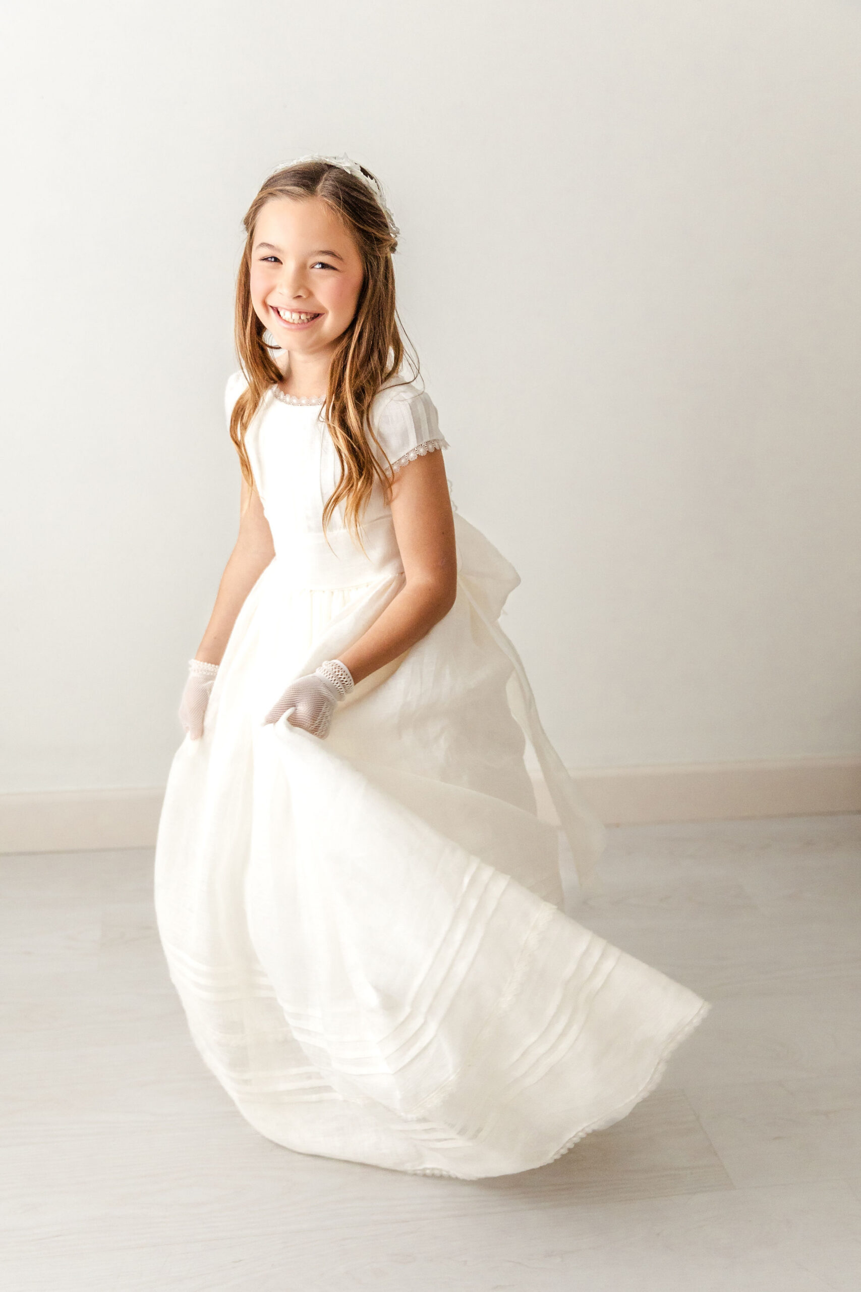 A giggling young girl dances in her long white dress in a studio