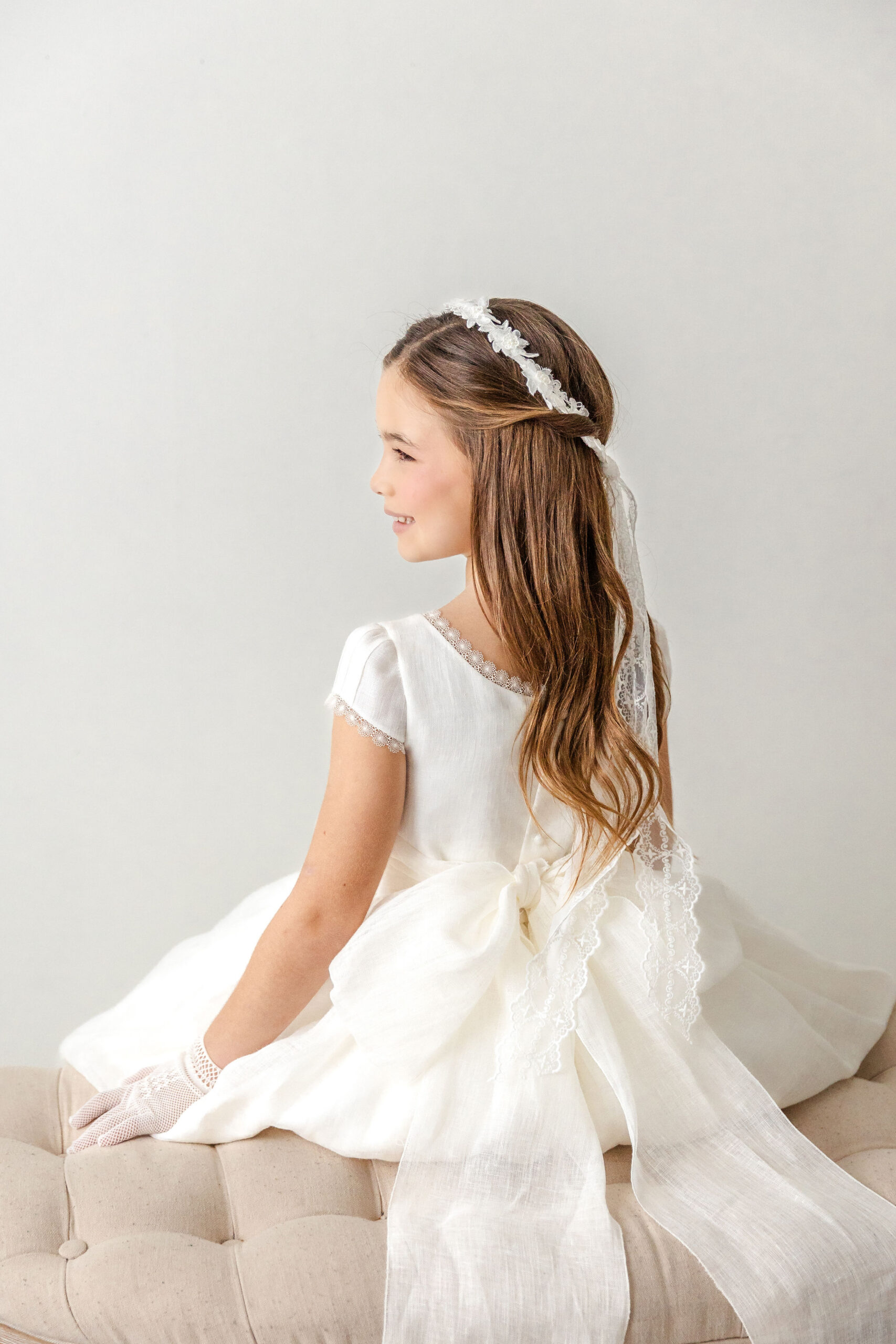 A happy toddler girl in her white first communion from cyberella baby dress on a bench