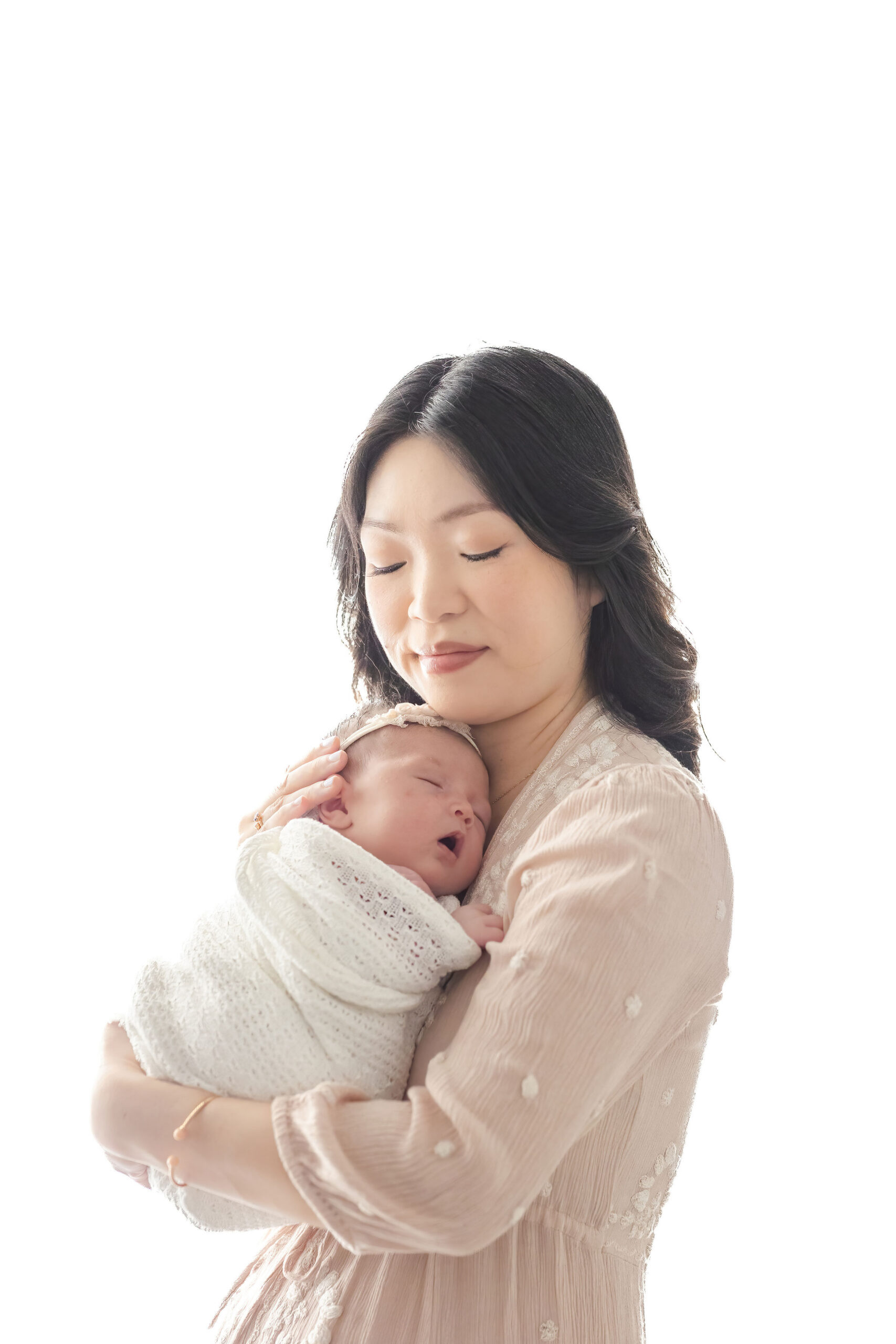 A smiling new mom snuggles her sleeping newborn daughter against her chest in a white swaddle thanks to harmony baby concierge