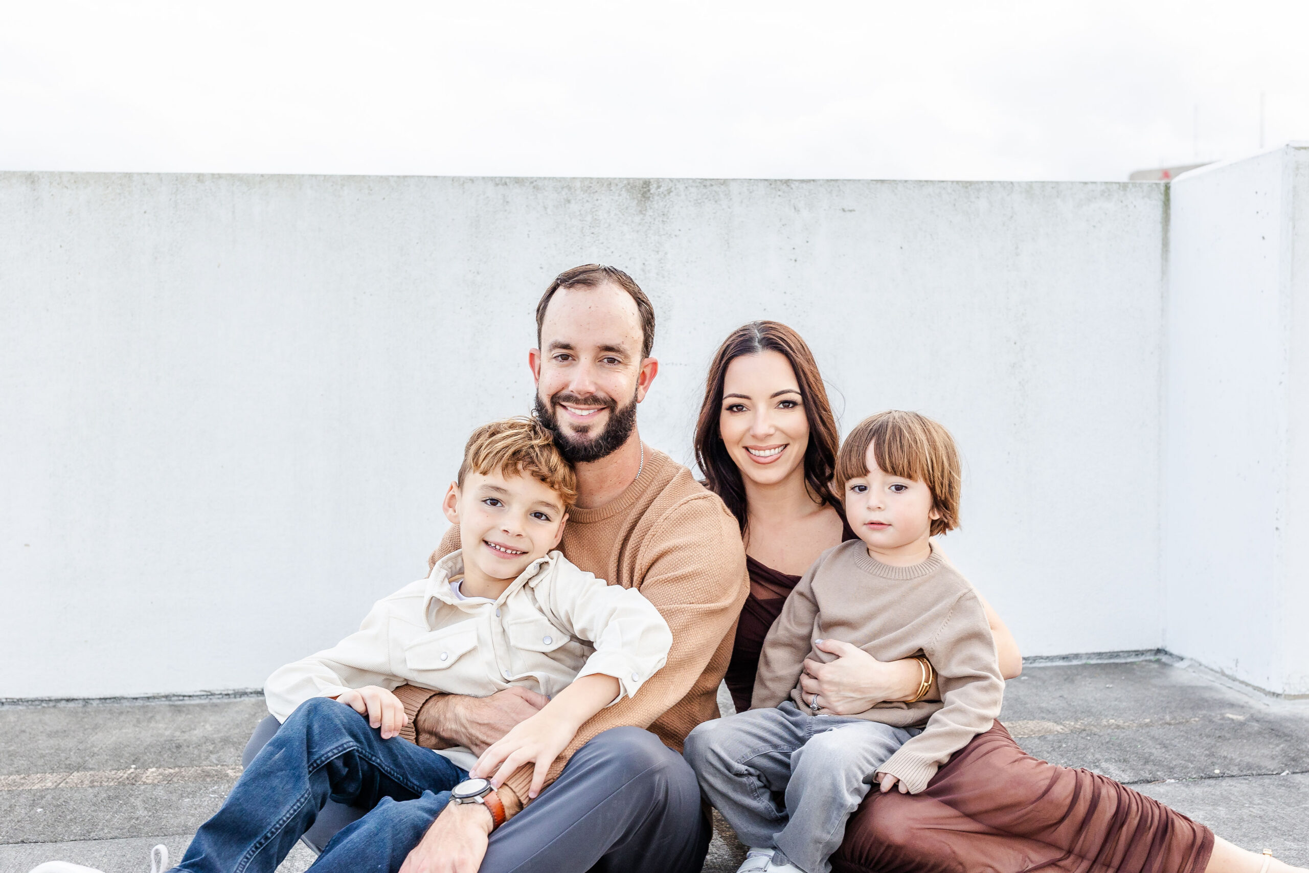 A happy family sit on the roof of a parking garage with two toddlers in mom and dad's laps after enjoying gyms with childcare in miami