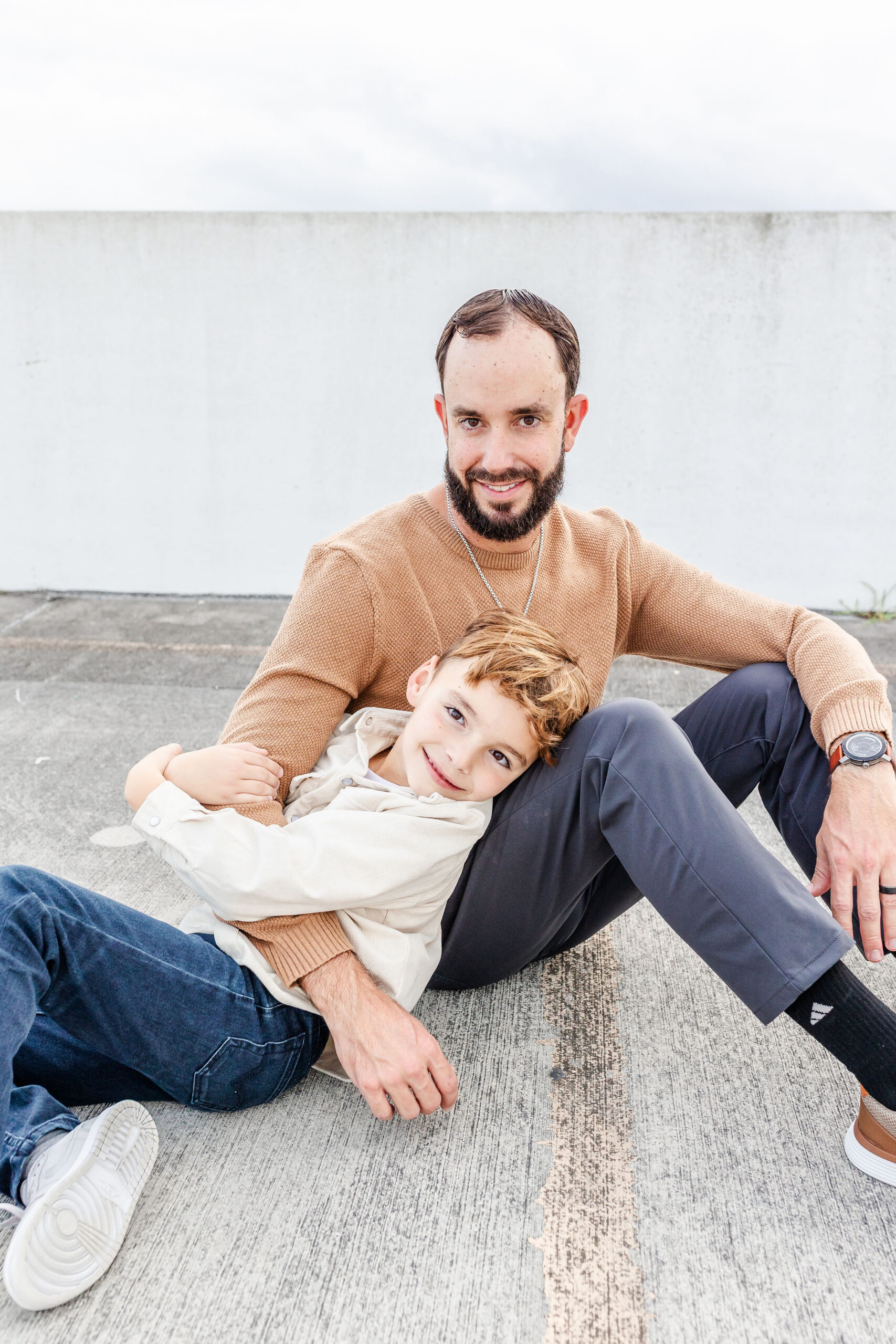 A young boy in a white shirt plays against dad's lap while sitting on a parking garage roof after finding gyms with childcare in miami